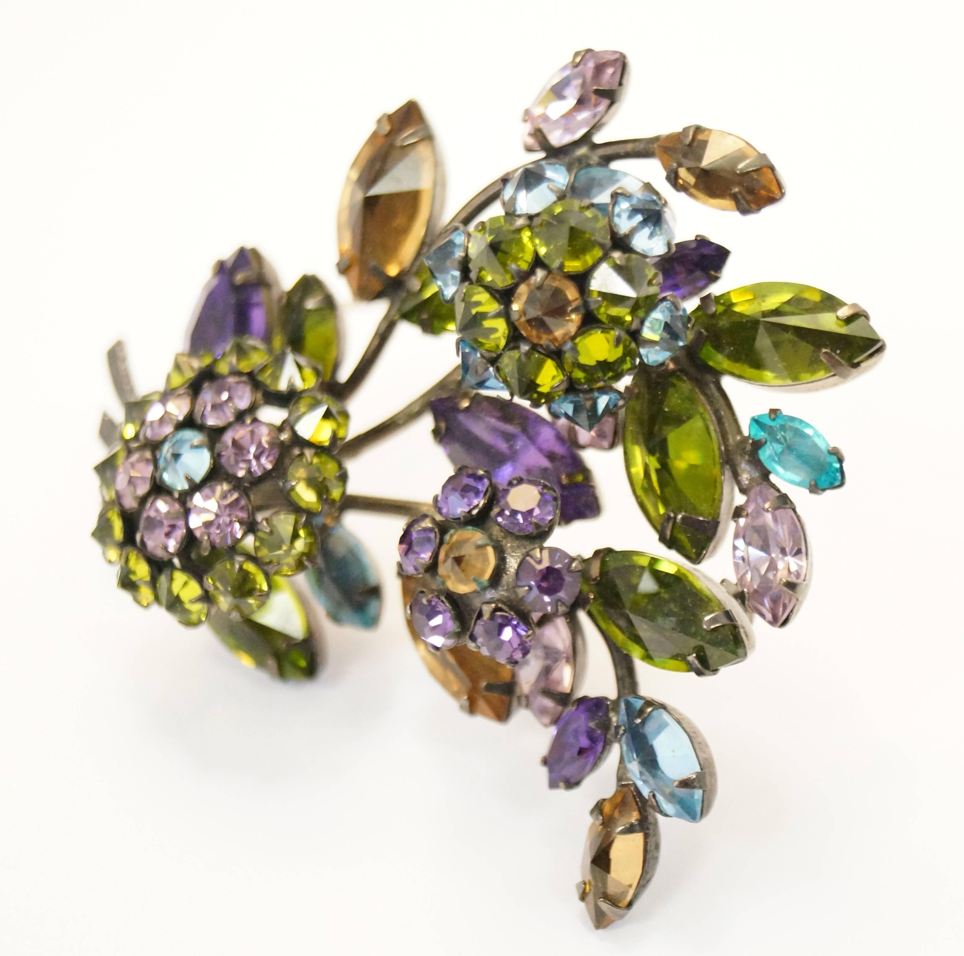 
Absolutely gorgeous vintage Schreiner floral brooch! This bouncy brooch is composed of green, orange, blue, and violet rhinestones in a floral bouquet formation. The three flowers are made of pointy inverted rhinestones, and are all set  into an