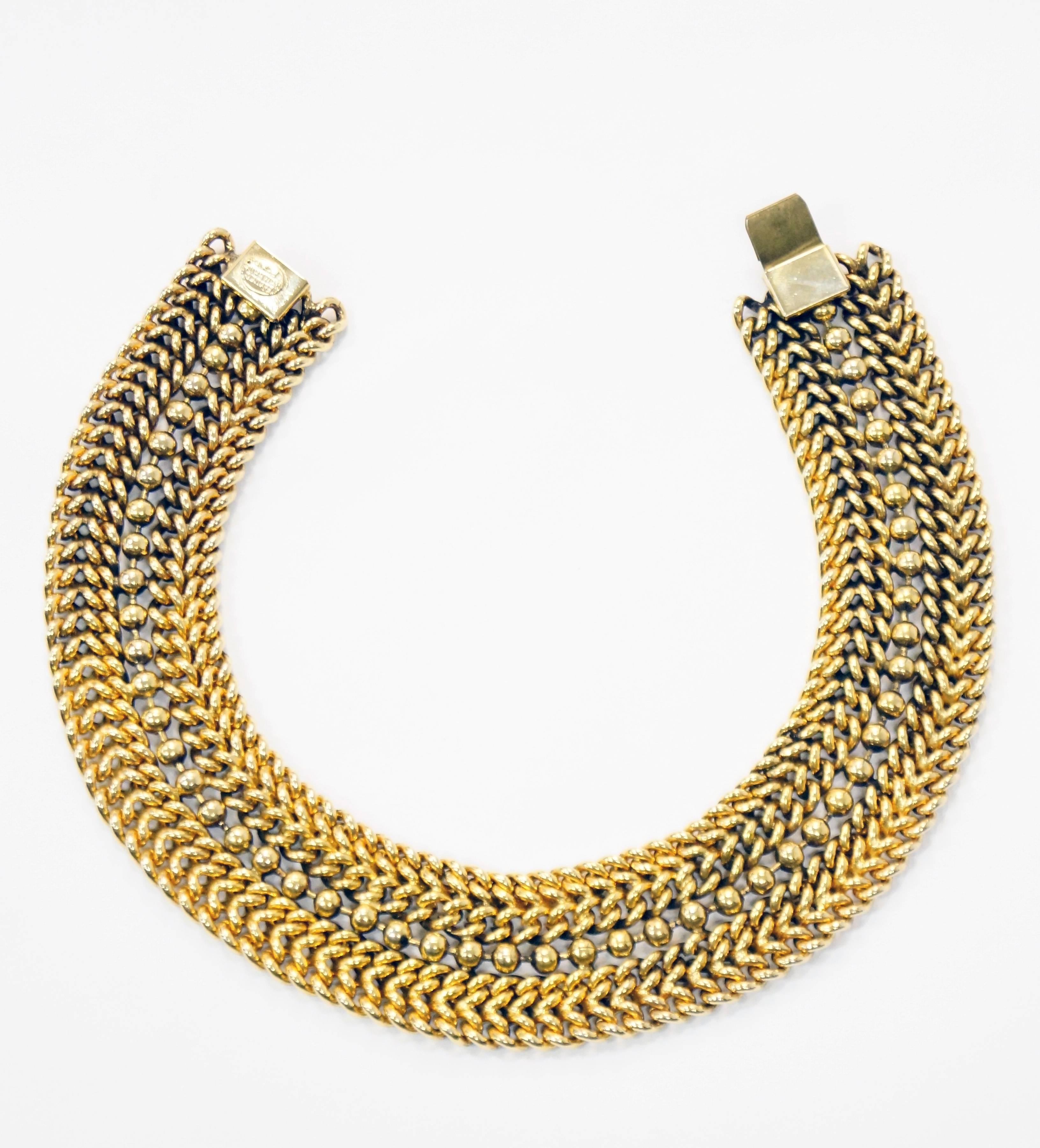 
This 1980s gold tone choker by Edouard Rambaud is absolutely fantastic! The choker is composed of a ball chain in the center of four rows of curb chains. The curb chains are fused together, making the necklace considerably dense, adding to its