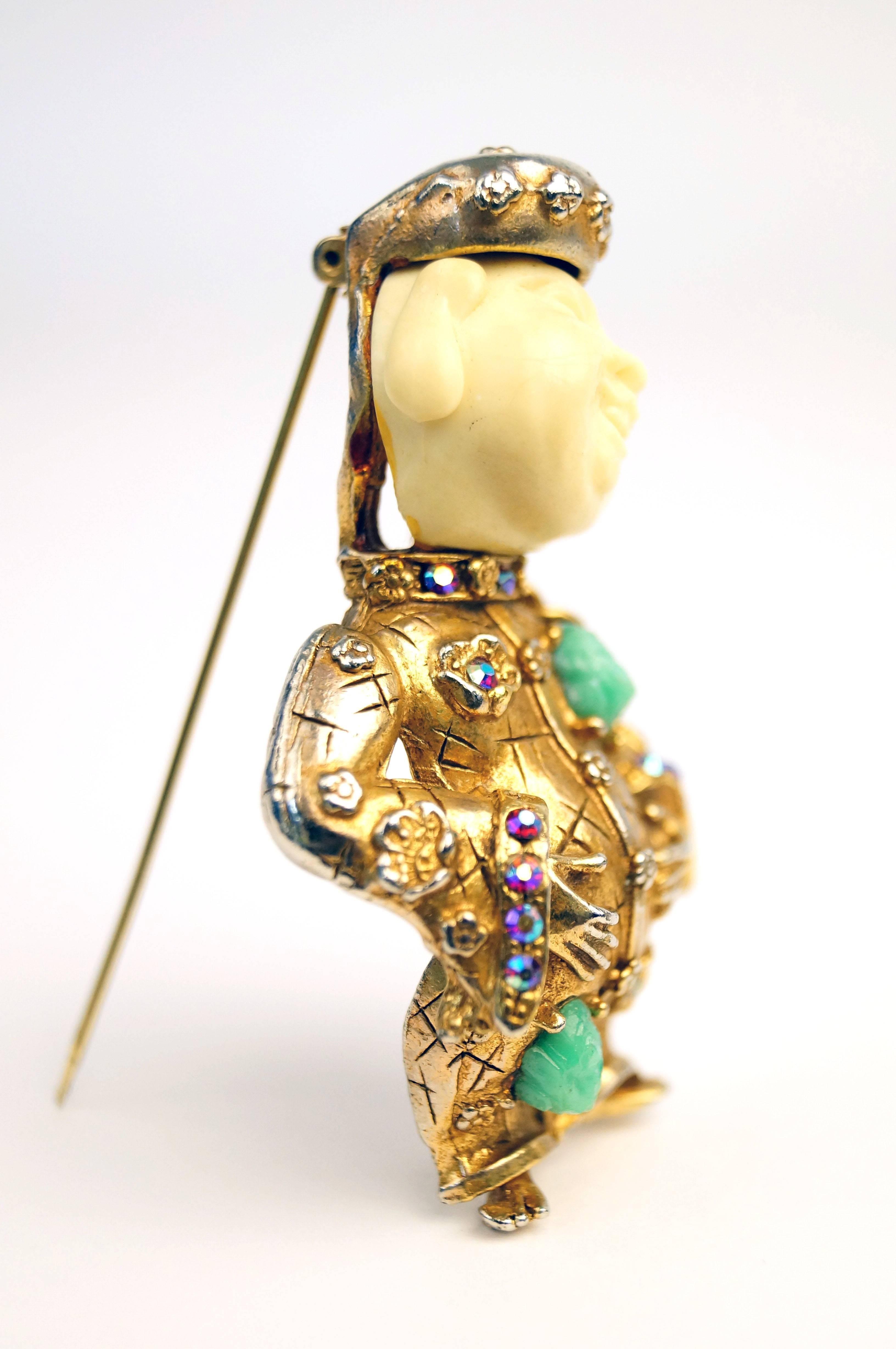 
This highly collectible and extremely fun vintage "laughing Buddha" brooch by HAR - Hargo Creations of NY, features a figure with a faux ivory head and gold-tone body. The robe is adorned with faux jade nuggets and malachite stones as