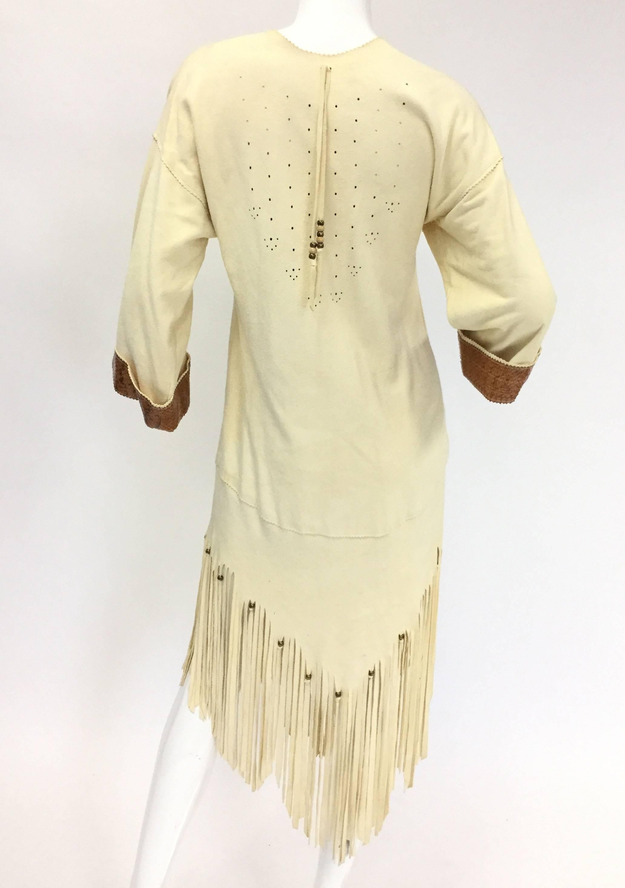 
This modern reinterpretation of the buckskin dress is absolutely striking! The light ecru chamois dress features caramel snakeskin detailing on the cuffs and collar, as well as a long fringed hem in an inverted triangle pattern. The fringe and the