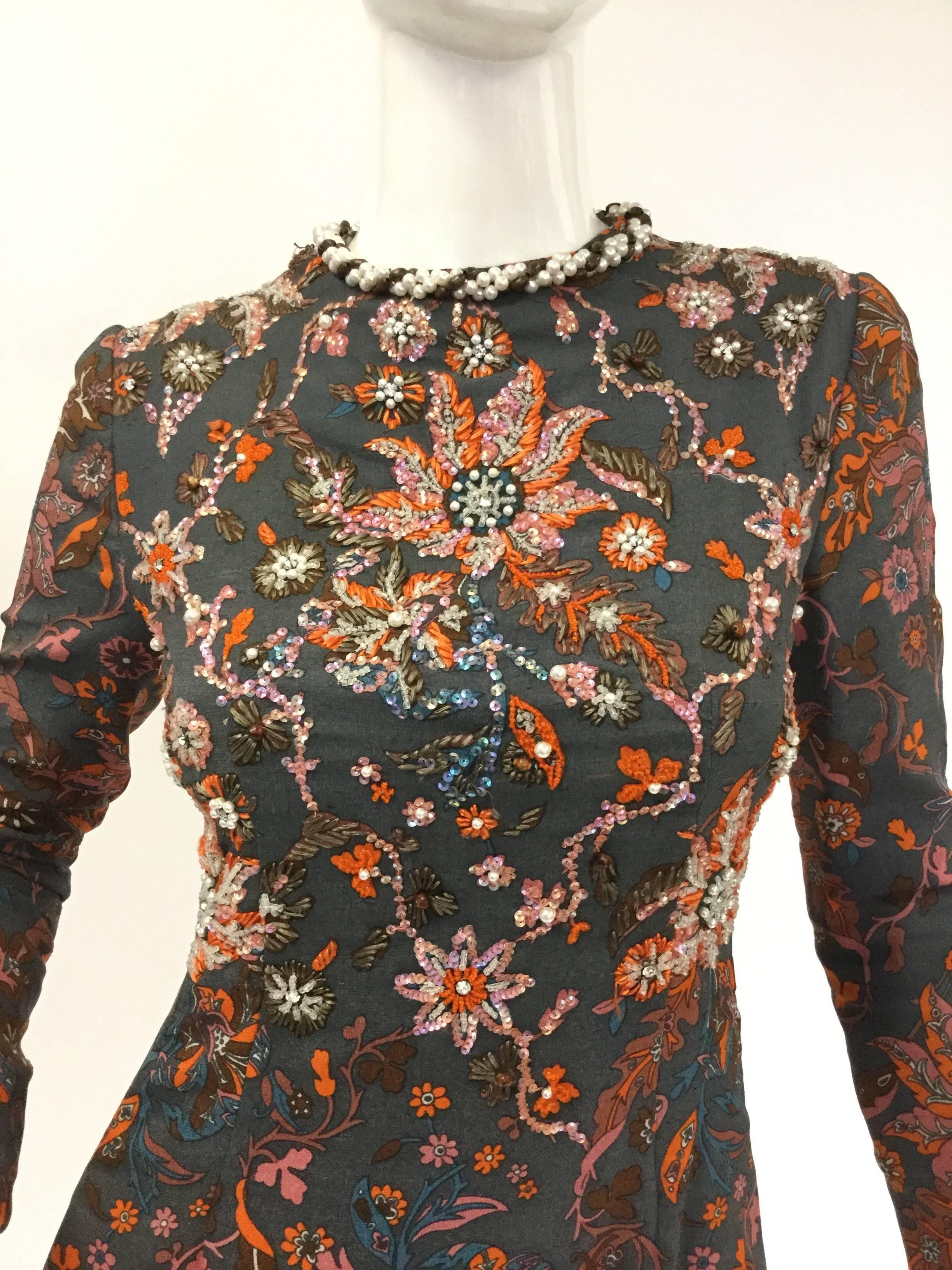 
This gorgeous beaded and sequined dress by George Halley is straight out of a fairy tale! The deep cyan background of the dress is host to a gorgeous potpourri of floral swirls and vines. The orange, pink, yellow, blue, and olive green flowers are