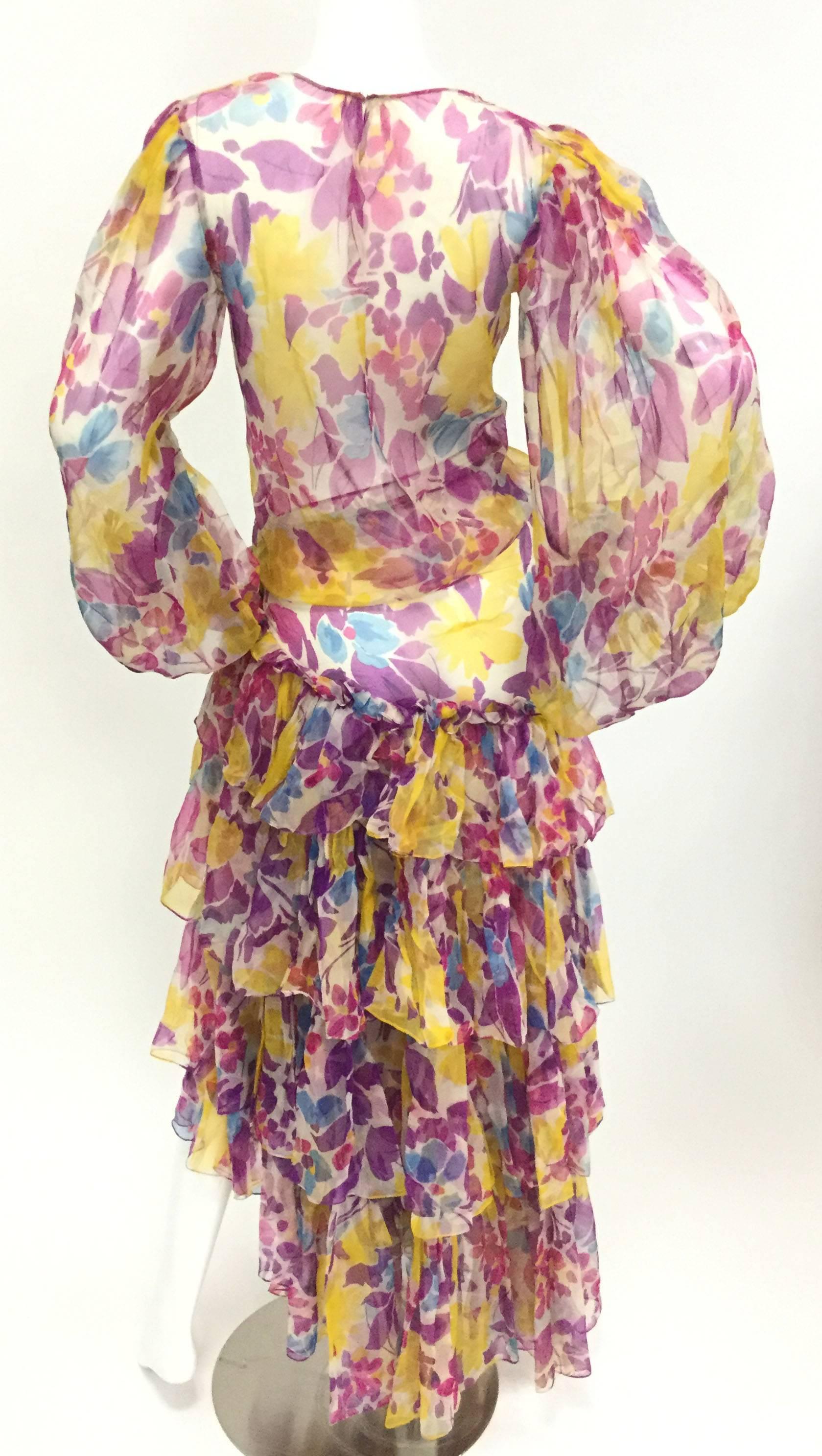 
This light and airy ensemble is an absolute dream! The sheer floral outfit is composed of a loose boat neck top with exaggerated bishop sleeves that taper at the wrist with an elastic cuff. The voluminous wrap skirt has multiple layers of sheer