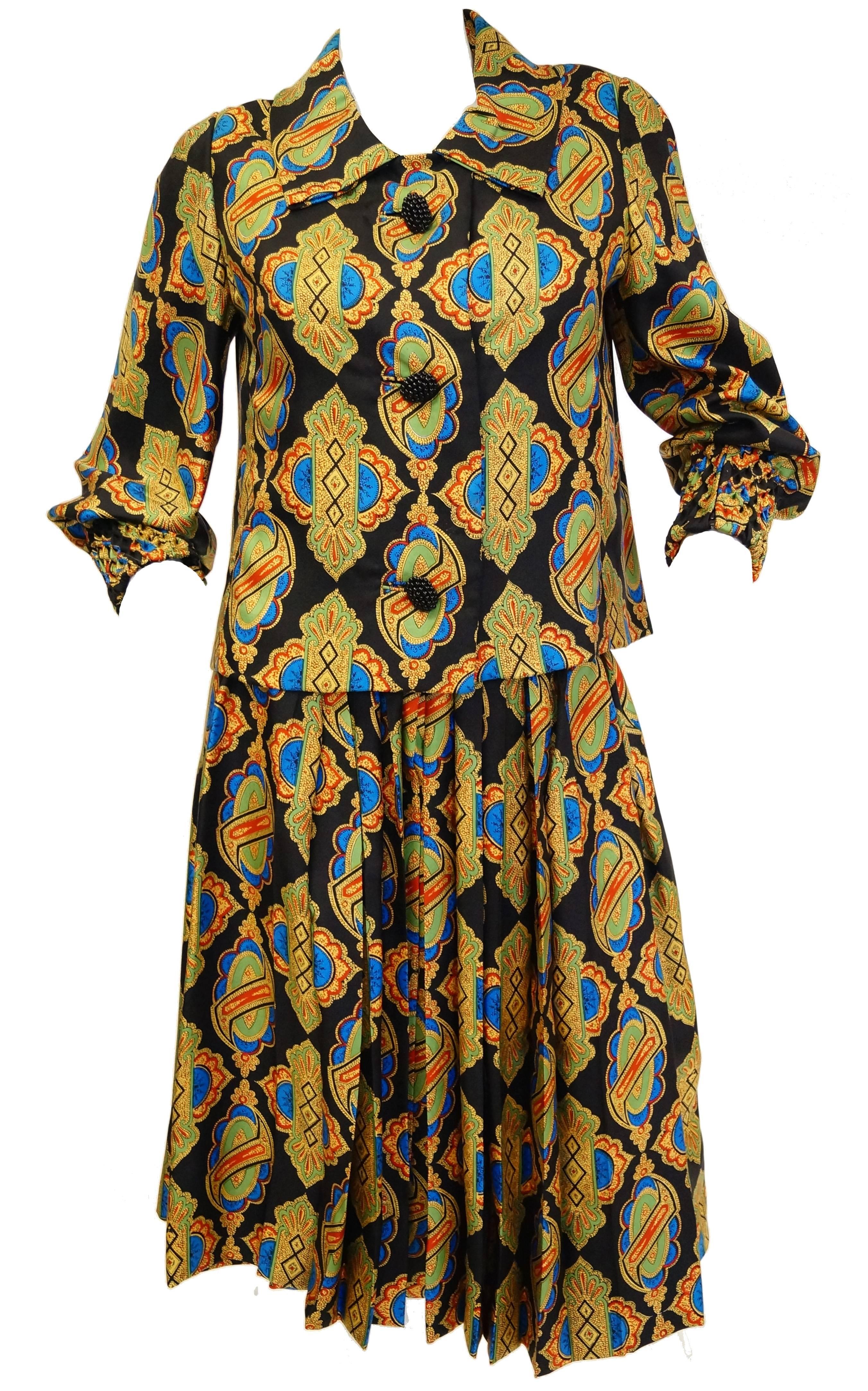 This 1970s ensemble by Galanos brings to mind the mosaic work in Venice's Palazzo Pisani-Moretta. The ensemble features ornate blue, gold, orange, and mint griccia print floral - like shapes on a black background. The silk ensemble is composed of an