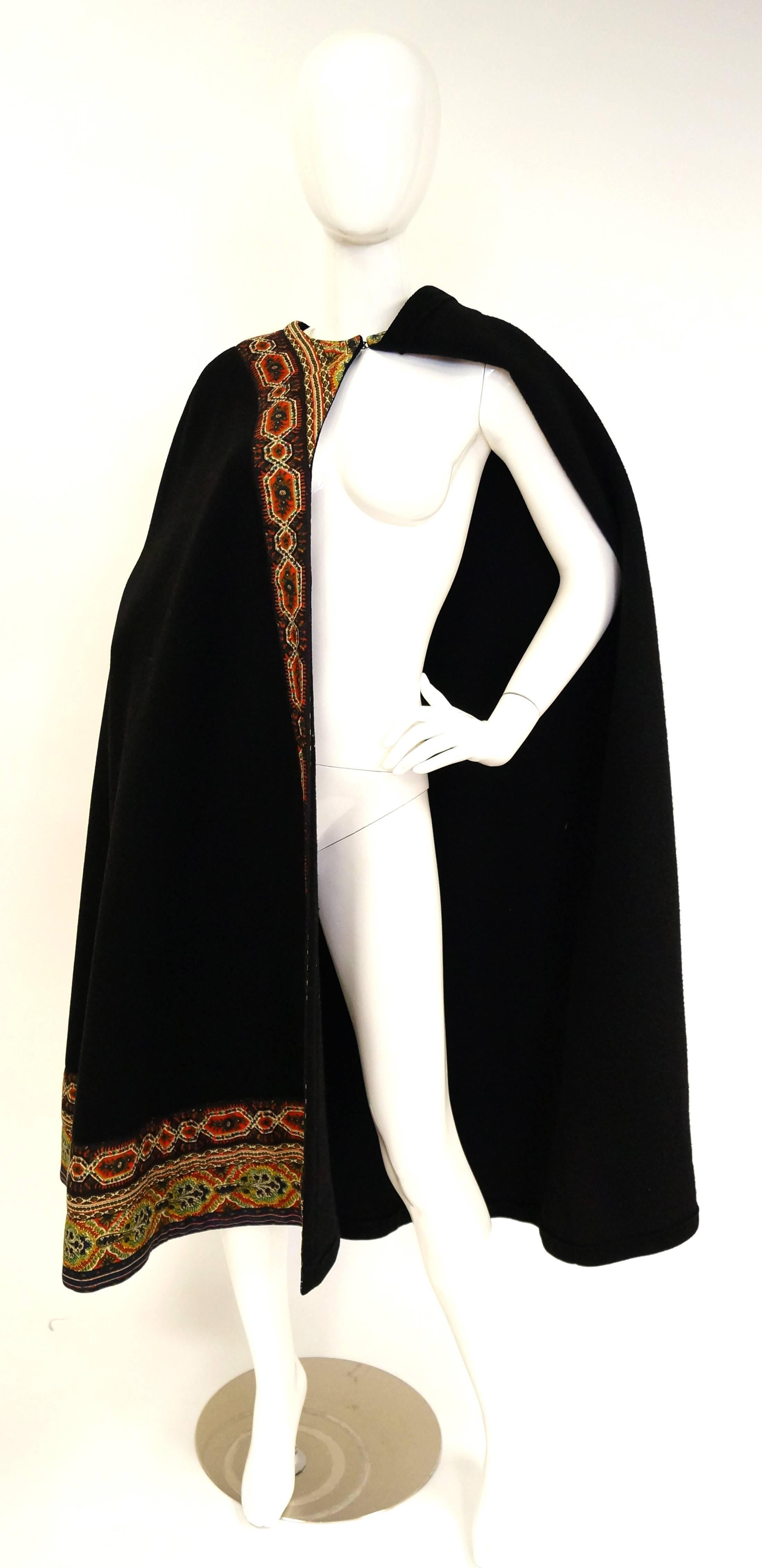 This mid century calf - length wool cloak by Oscar de La Renta is an absolute delight! The cloak is made of soft, thick black wool, and features a bright and colorful bohemian trim. The floral and geometric trim extends around the collar and down