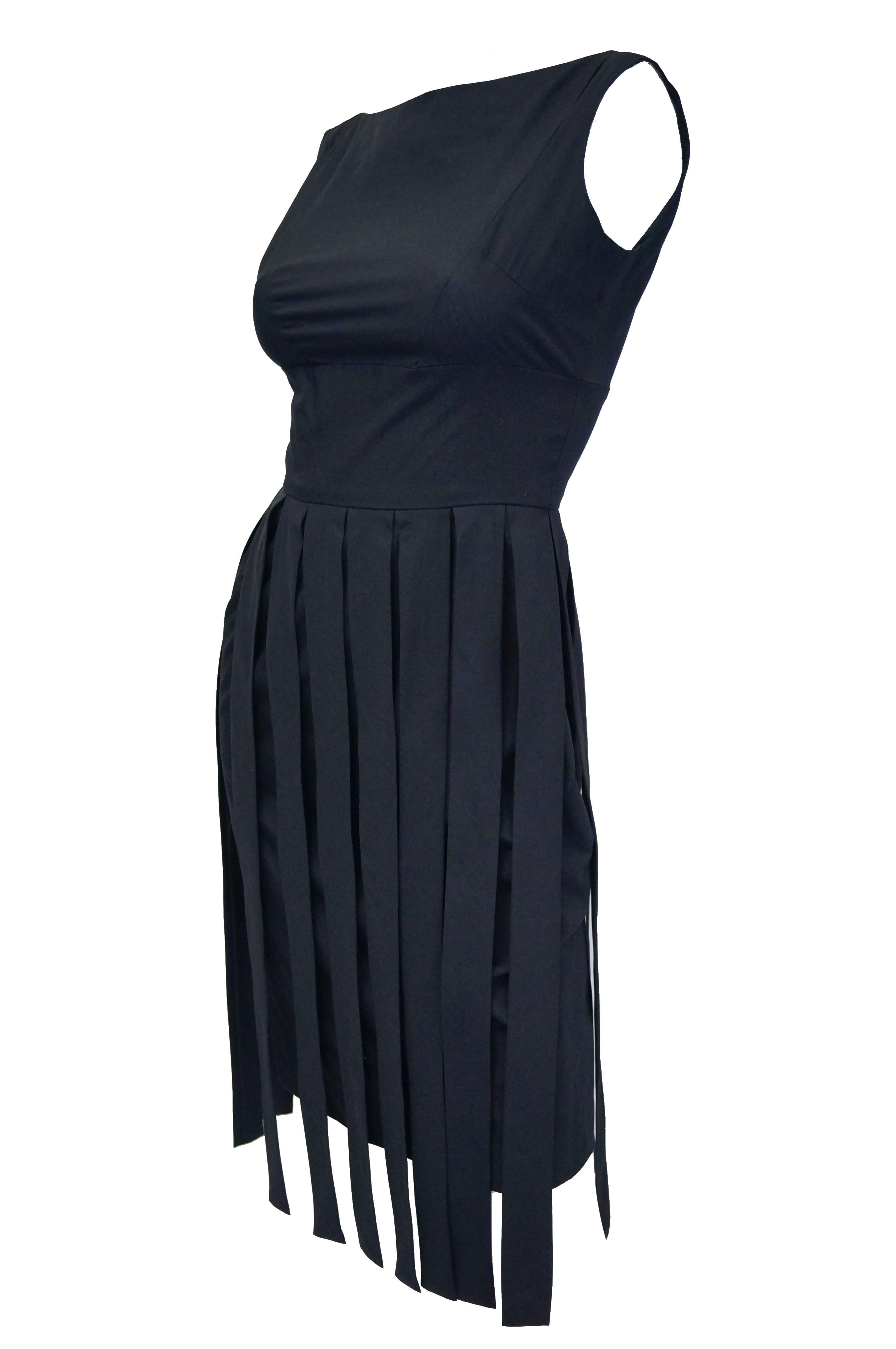 Beautiful body-skimming black cocktail dress by Jaques Heim! The sleeveless dress features a bateau neck with a triangular plunge back. The pencil skirt of the dress is layered below strips of fabric, bringing to mind a cleanly deconstructed knife