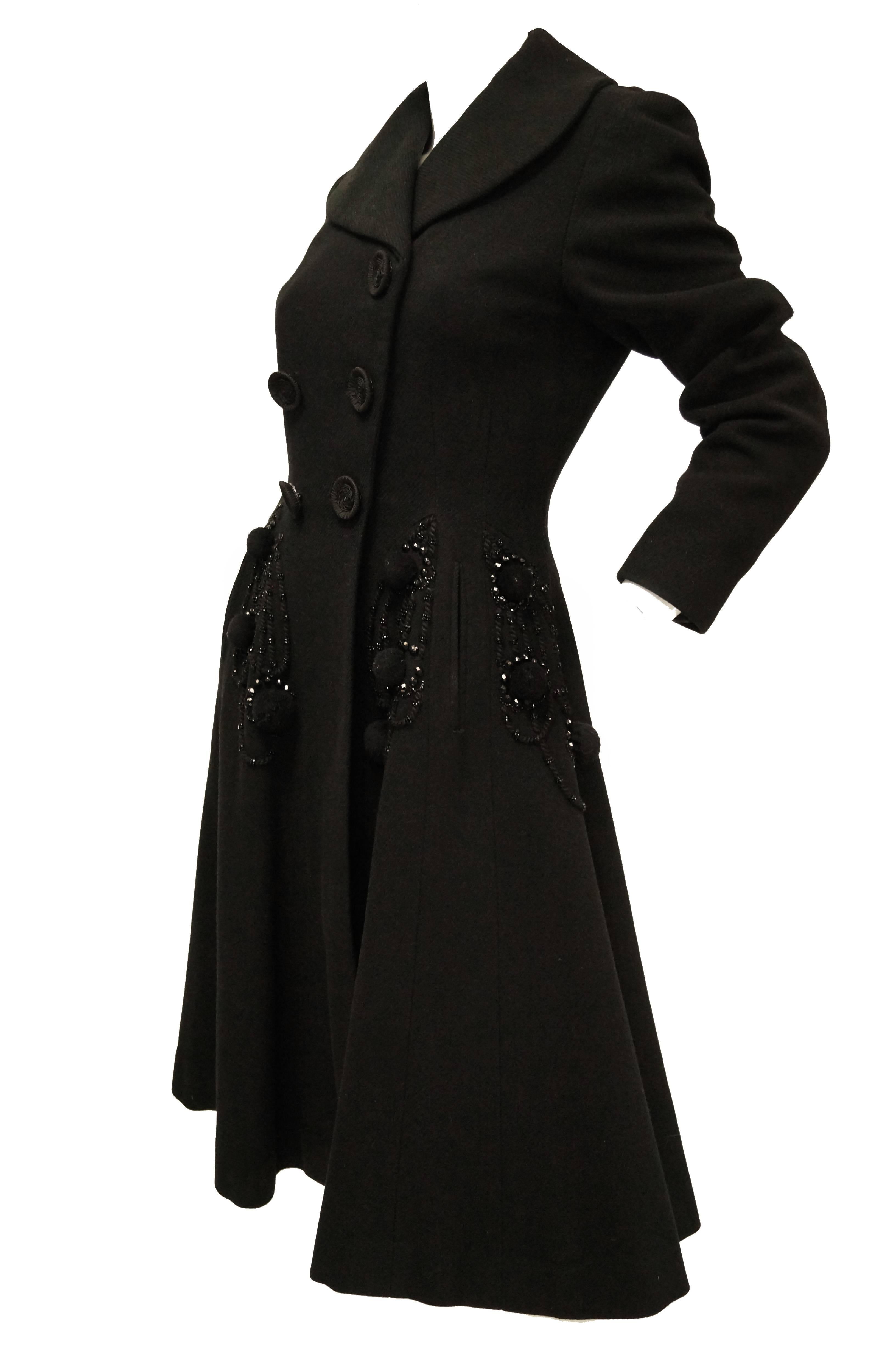 Absolutely gorgeous! This black wool coat by Agnes - Drecoll hits just below the knee and has a fit and flare silhouette, giving the tea length dress a very feminine outline. The coat has a shawl - like collar, is double breasted and features