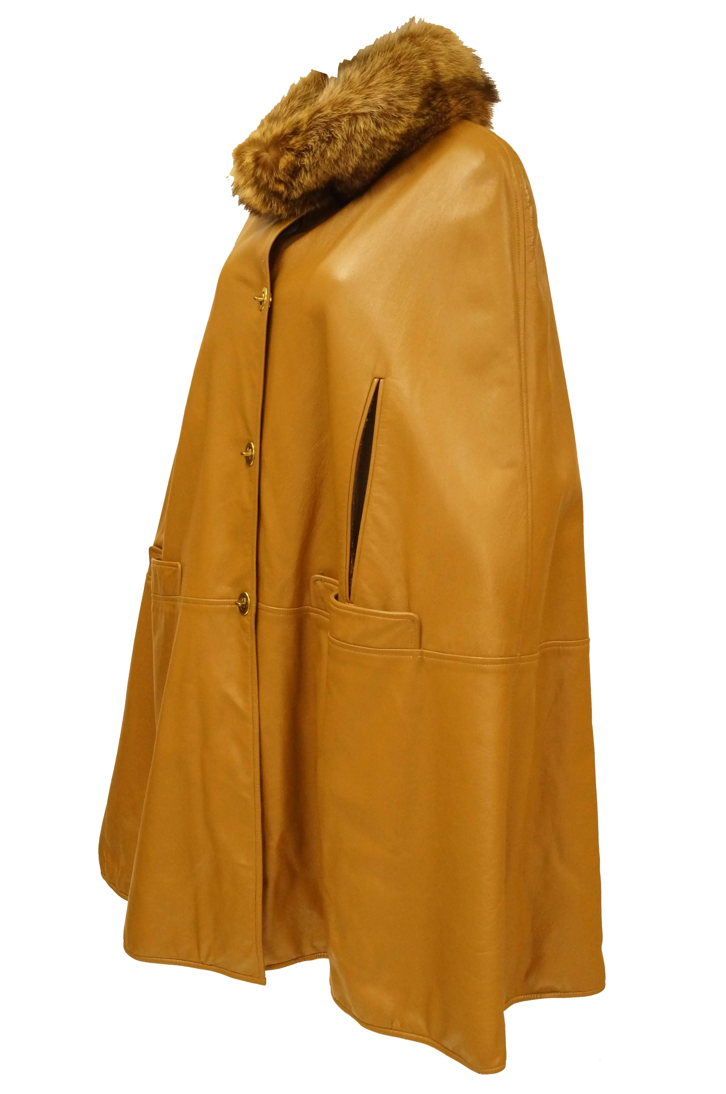 Protect yourself from the nose-bitingly cold winds of winter with the plush fur collar on this fantastic camel colored leather cape by Bonnie Cashin. The cape itself -
with its glossy, smooth finish - is stunning. The cape is thigh-length, with arm
