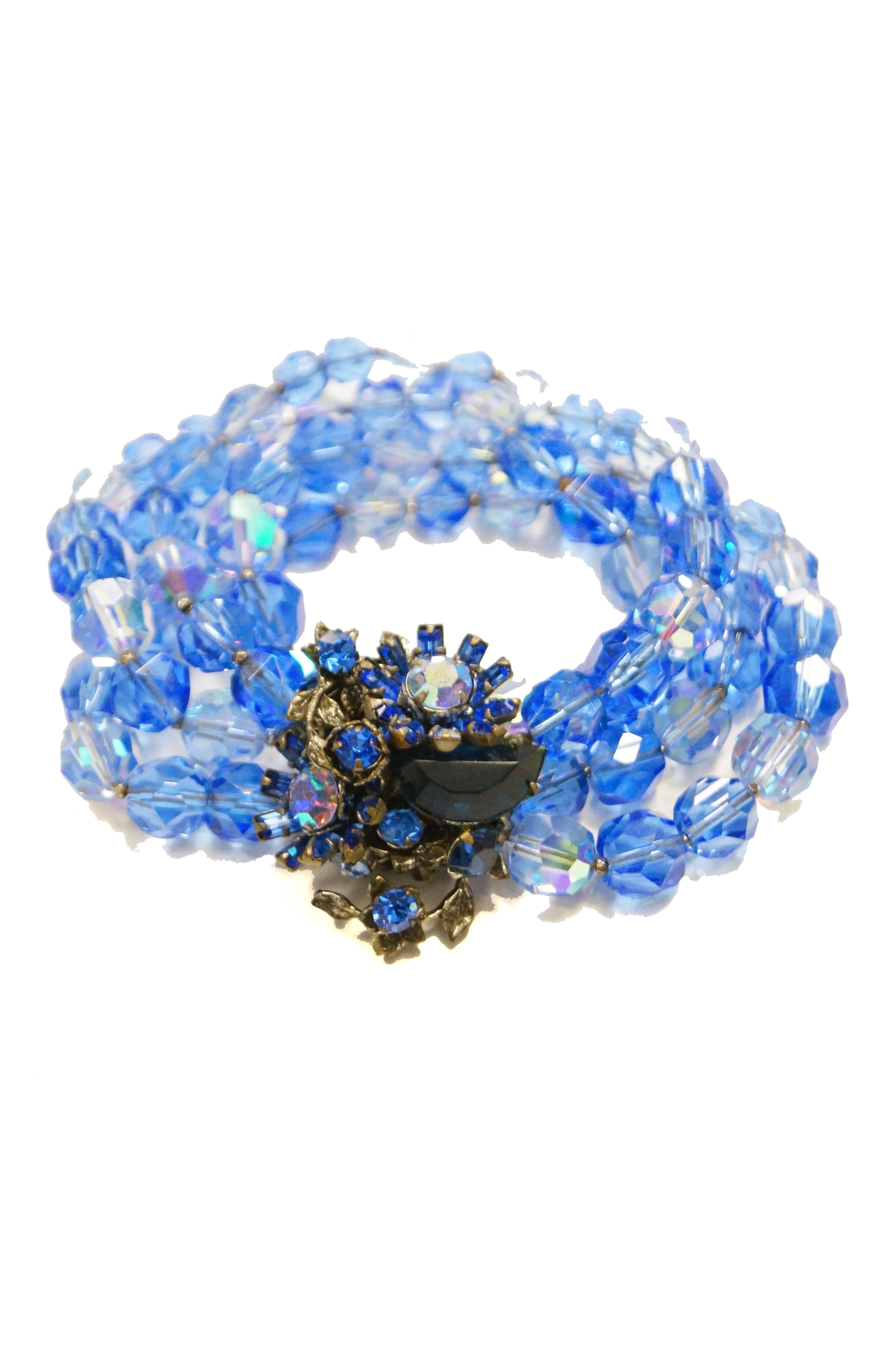 Amazing cobalt blue glass bead demi parure consisting of a brooch and bracelet. The multi strand bracelet is composed of multifaceted blue and clear iridescent glass beads held together by a bronze clasp with iridescent rhinestone floral details.