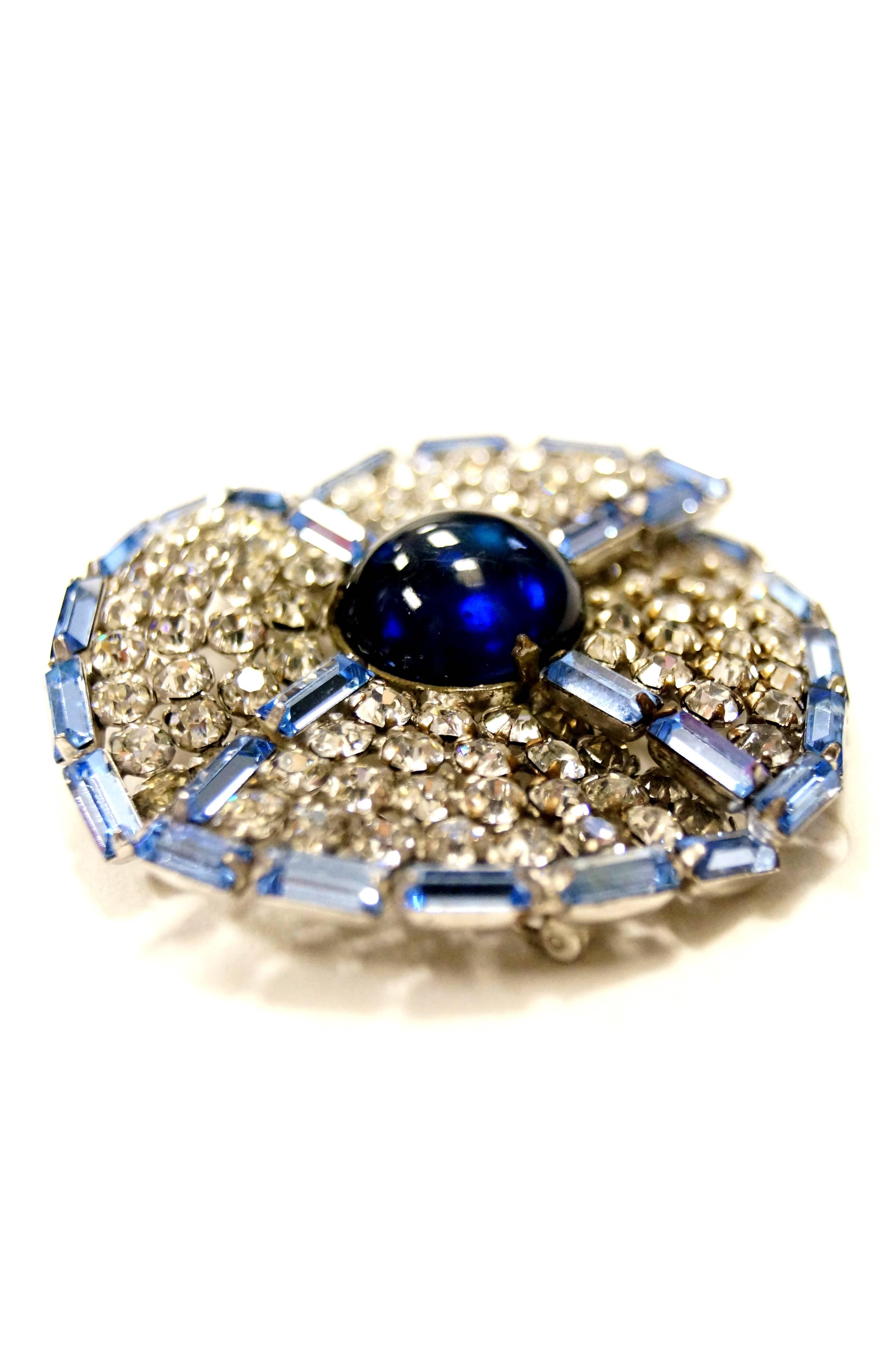 Beautiful 2 inch round rhinestone brooch in a pinwheel shape!  This Hattie Carnegie brooch is composed of several overlapping rhinestone wedges. The wedges are bordered in blue baguette rhinestones that hold in the small round multifaceted clear