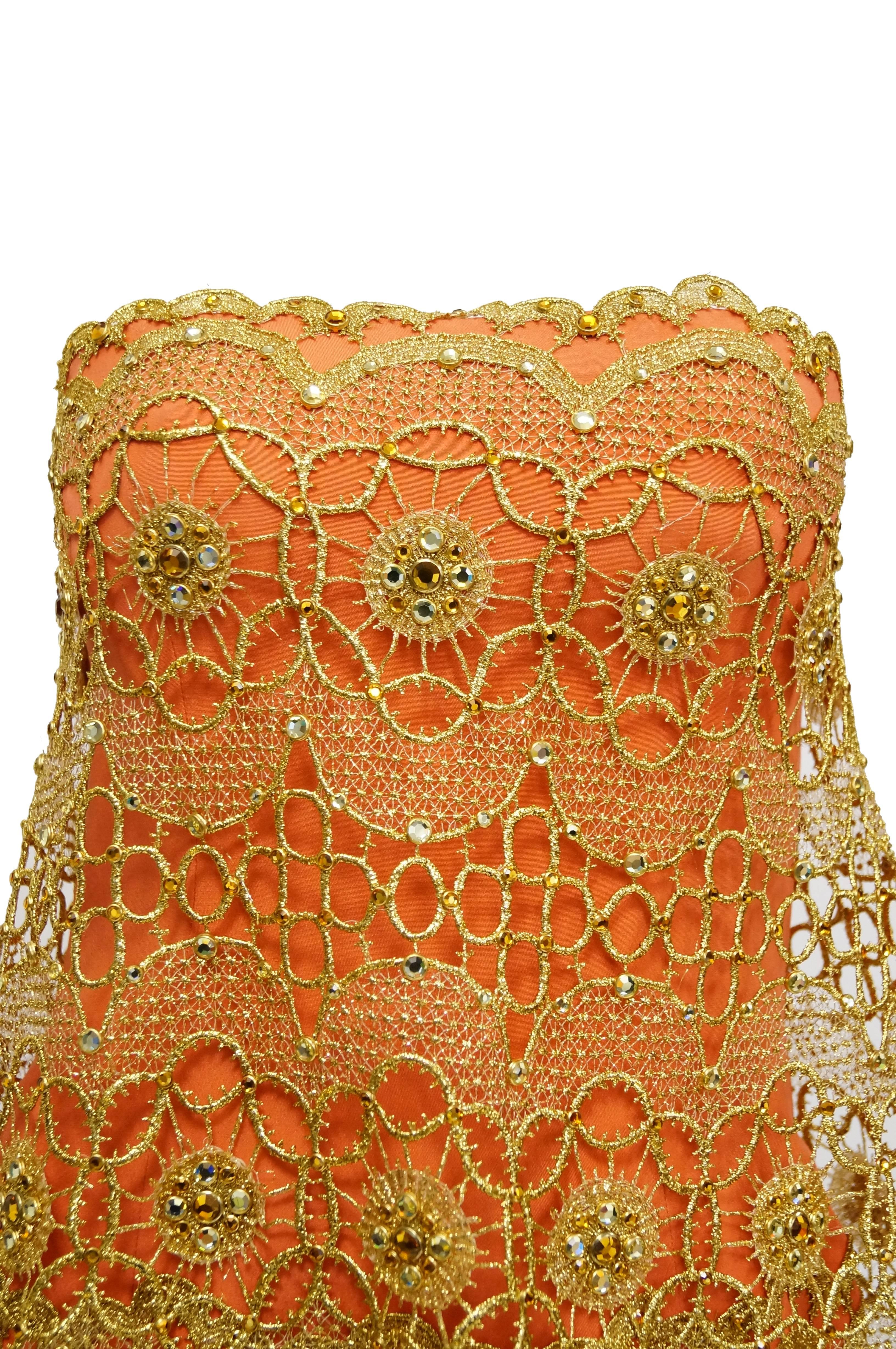 Tangerine form fitting cocktail (or party!) dress by Bob Mackie. The dress is thigh-length and consists of a tangerine fitted sheath dress under layers of gilded lace. The lace extends out from the neckline and the hip. The lace is geometric and