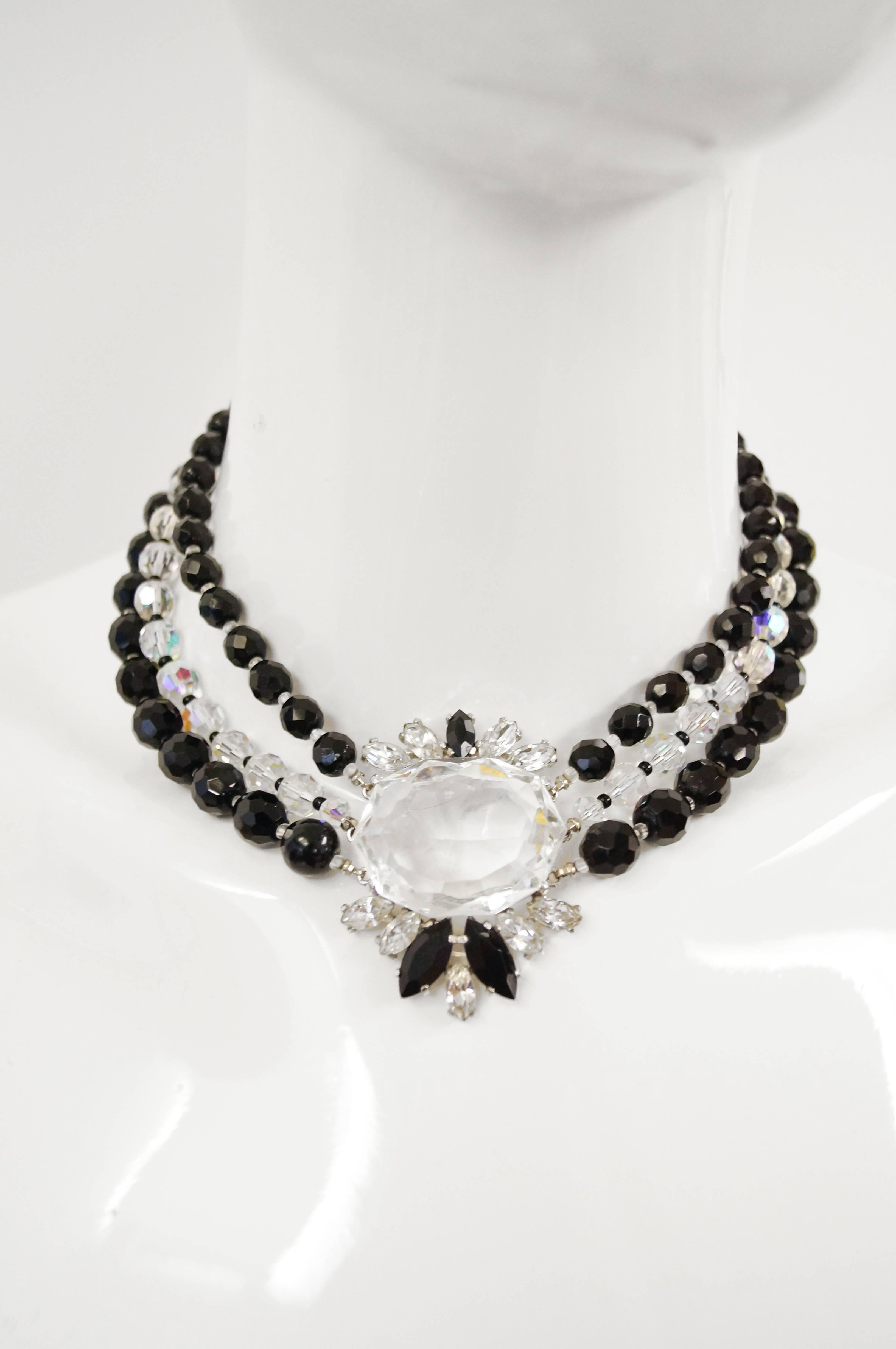 This black, iridescent, and clear rhinestone necklace by Elsa Schiaparelli is absolutely luminous! The focal point of the necklace is a large, clear, radiant, flat, multifaceted center stone surrounded by black and clear rhinestones. The center