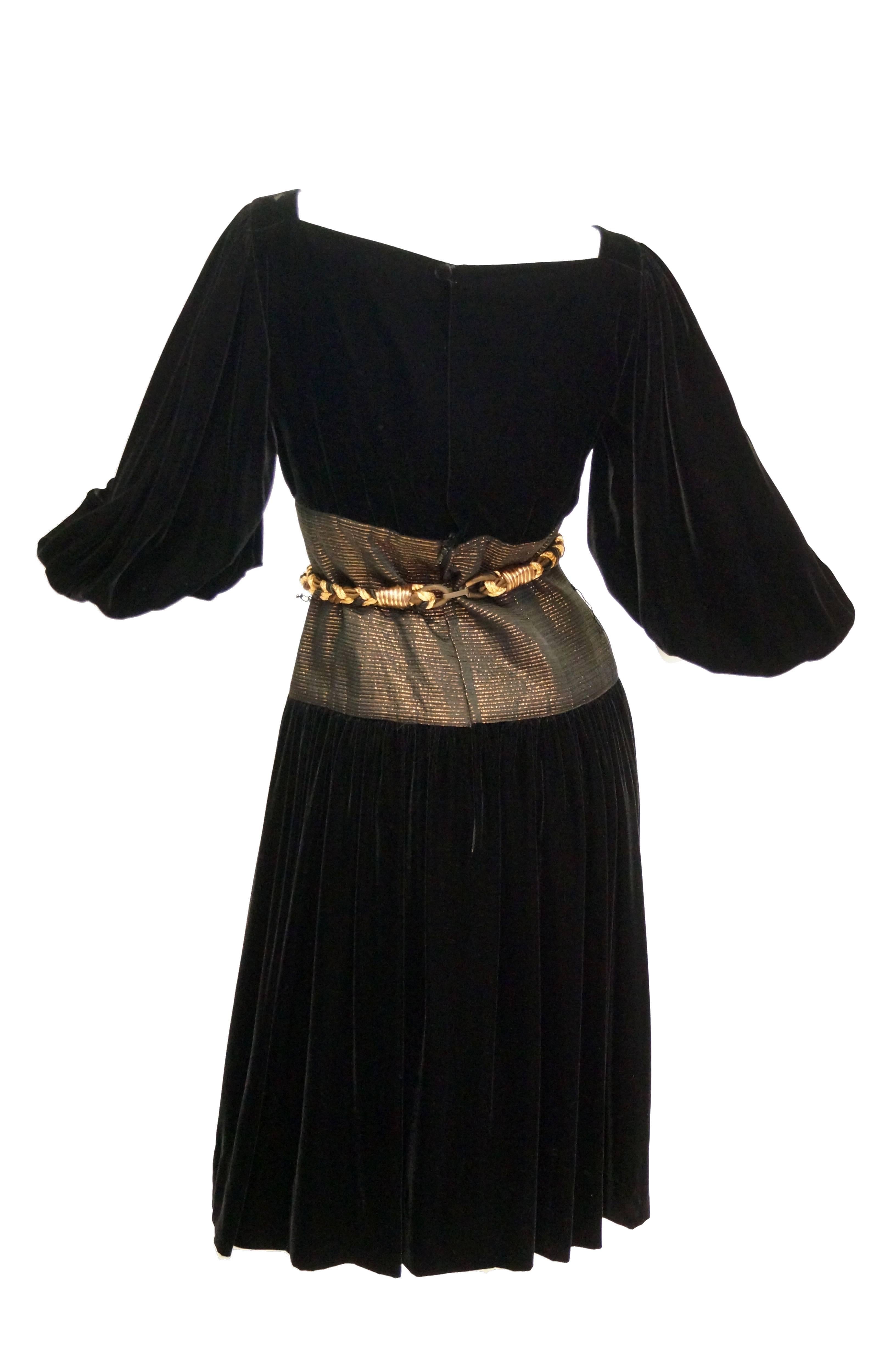 Elegant evening dress in sumptuous velvet with brilliant metallic details by Adele Simpson. The dress falls just above the knee, has a wide bateau boat neck, and 3/4 length sleeves. The sleeves are voluminous and gather at the elbow. The dress