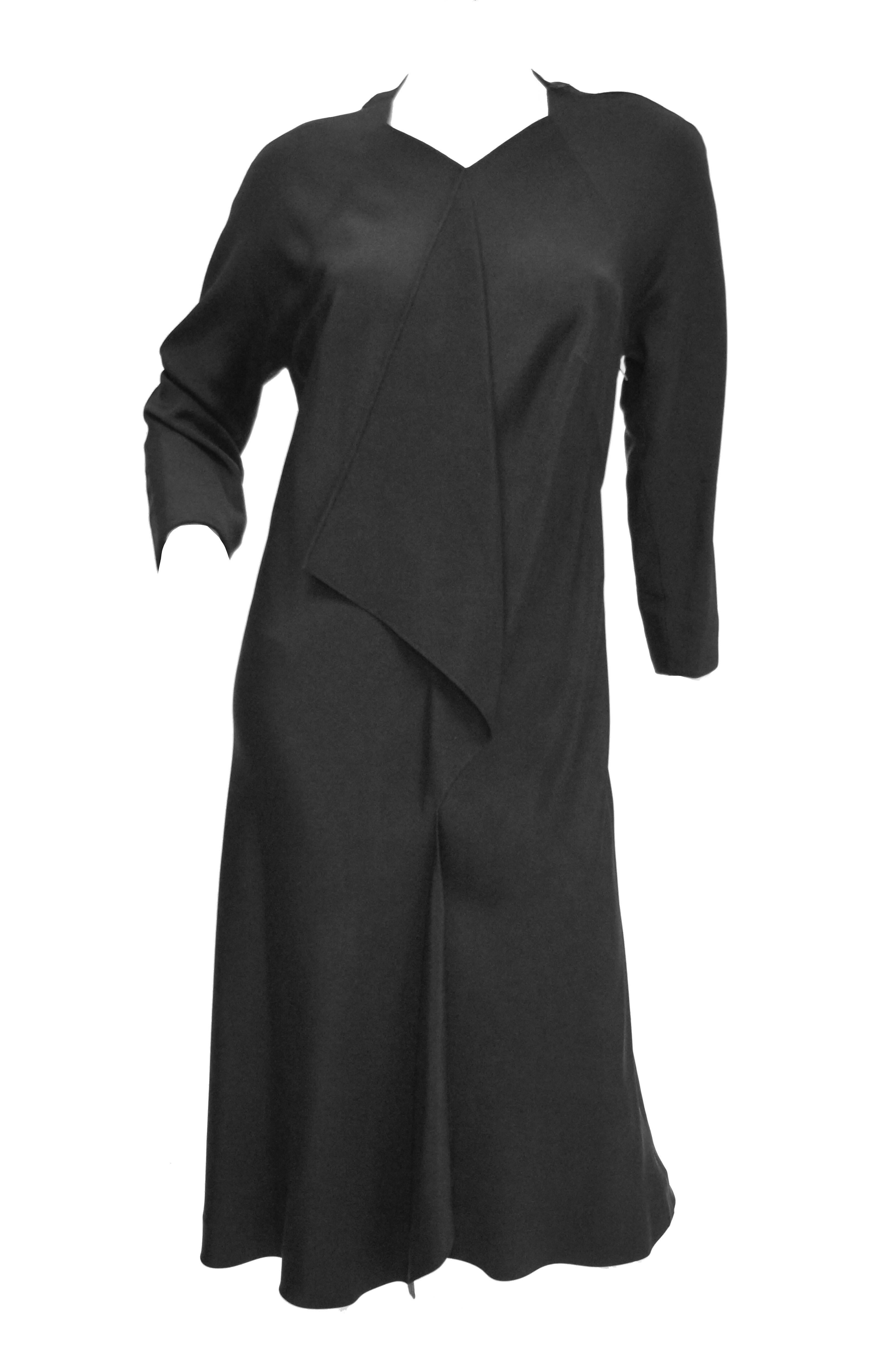 Gorgeous black silk faille evening dress by Madame Gres. The knee length dress is sleek, with a loose body - skimming silhouette, long sleeves, and a high, diamond cut neckline. The sleeves have a dolman - like cut. The dress has a front center seam