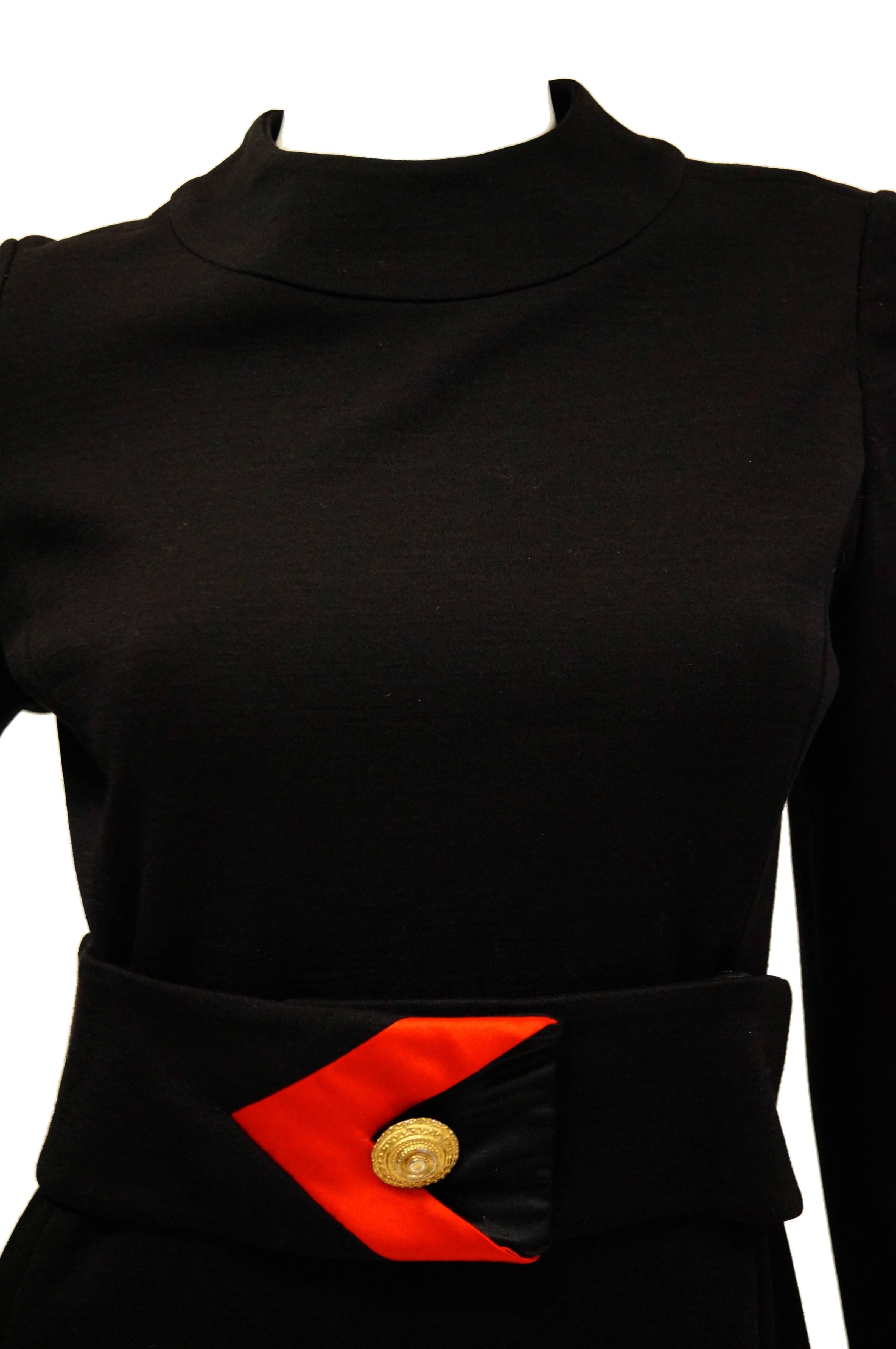 Striking black and red knit dress by Muriel Reade for Joseph Stein. The dress features a loose A - line silhouette with long sleeves and a tight jewel collar. The narrow waist of the dress is accented by a wide black belt with buckle - like arrow