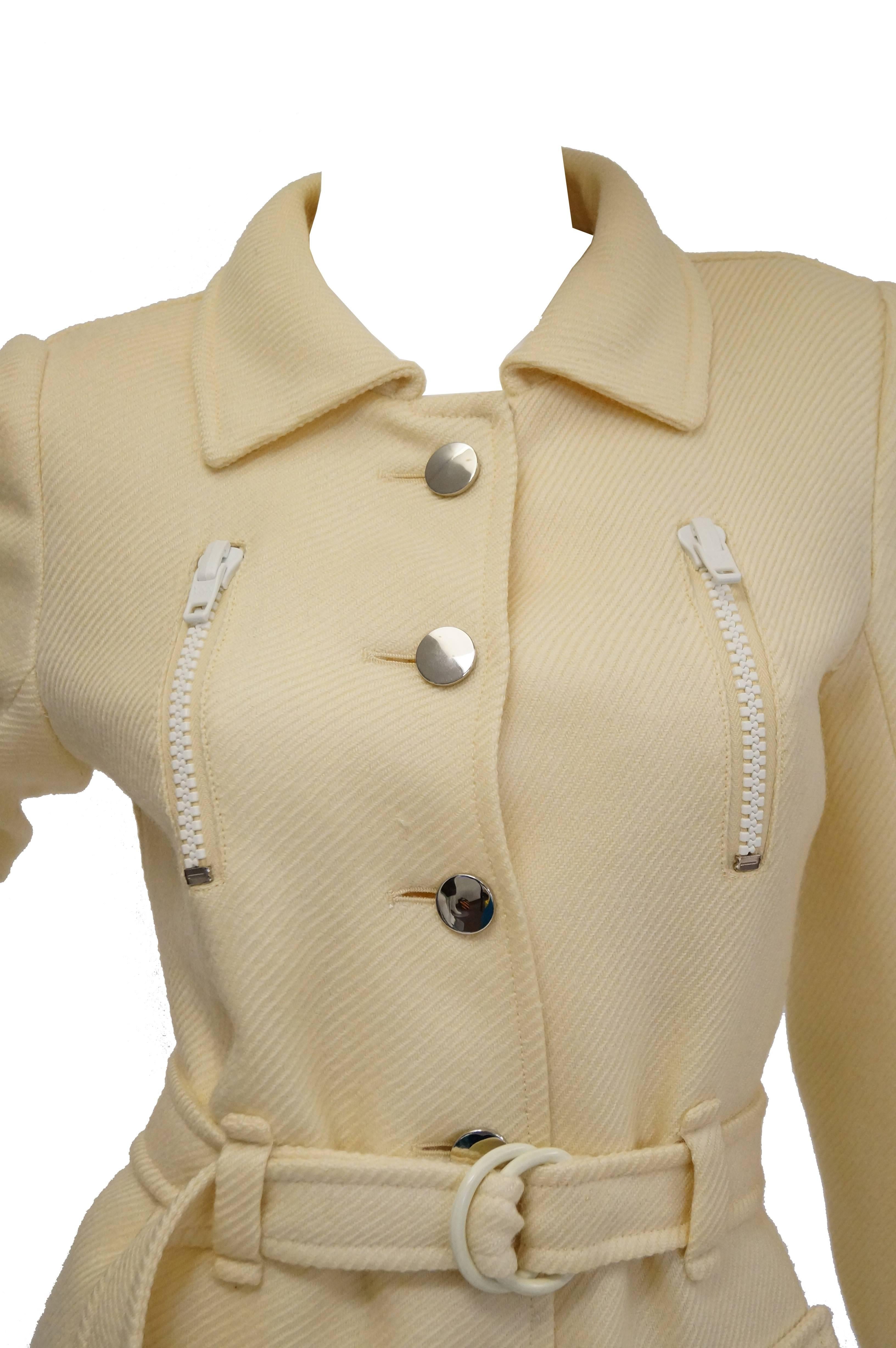 Cream mod coat by Courreges. The coat has a flat collar, long sleeves, and hits hits just below the knee. The sleeves are cuffed and have the same chrome buttons features throughout the coat. The coat is single breasted and features ten large,