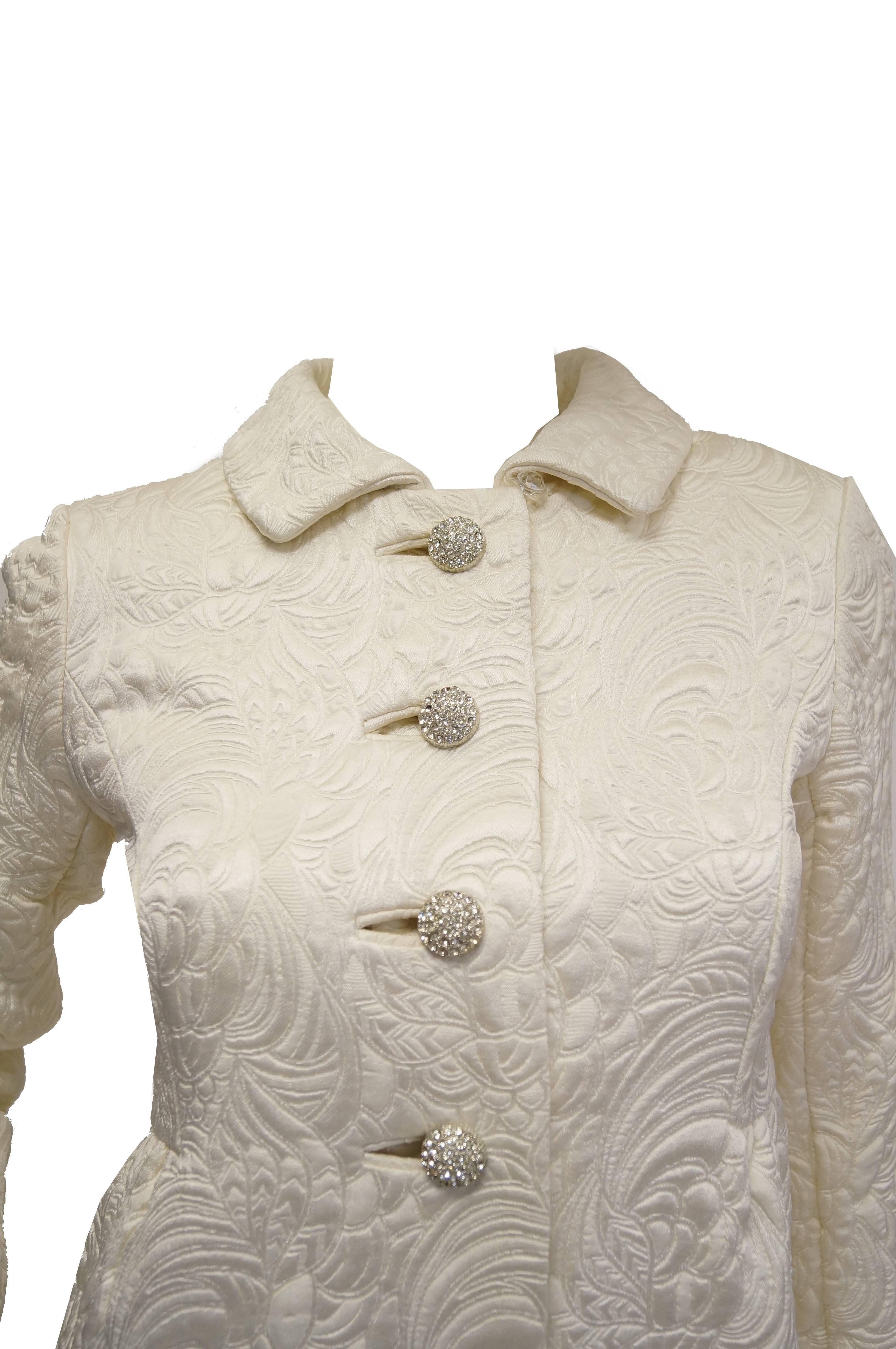 Splendido cappotto color avorio con trapuntatura a volute floreali tipo broccato. Il cappotto ha una silhouette ampia a campana con busto aderente, maniche lunghe e collo piatto. Il cappotto monopetto presenta quattro favolosi bottoni assolutamente