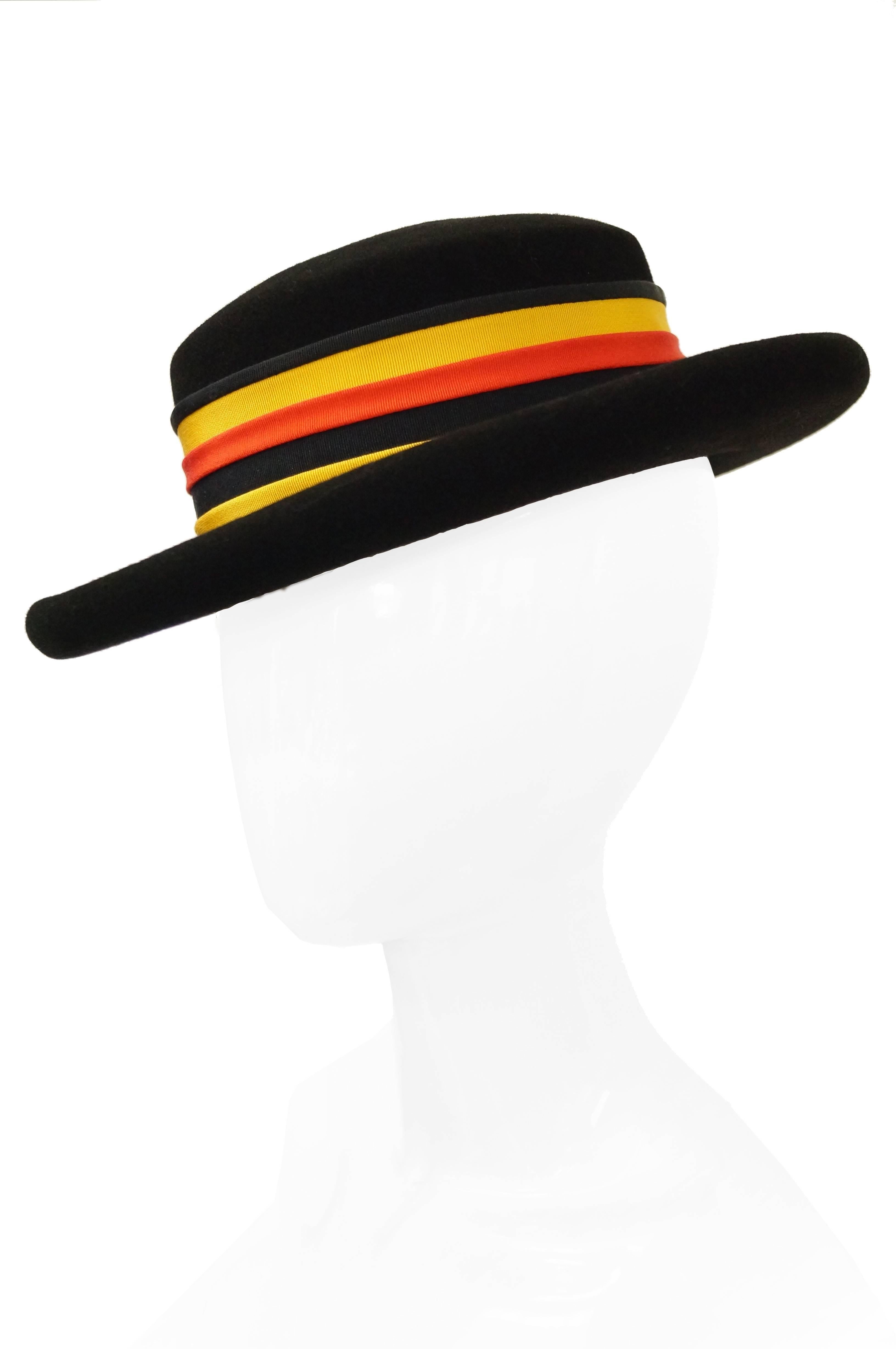 Understated medium width brim hat by Adolfo. The hat is somewhat similar to a boaters hat, although with a thick curled brim, and a circular, rounded crown. The hat is topped off with a wide ribbon band in red, orange, and black. Spectacular!


