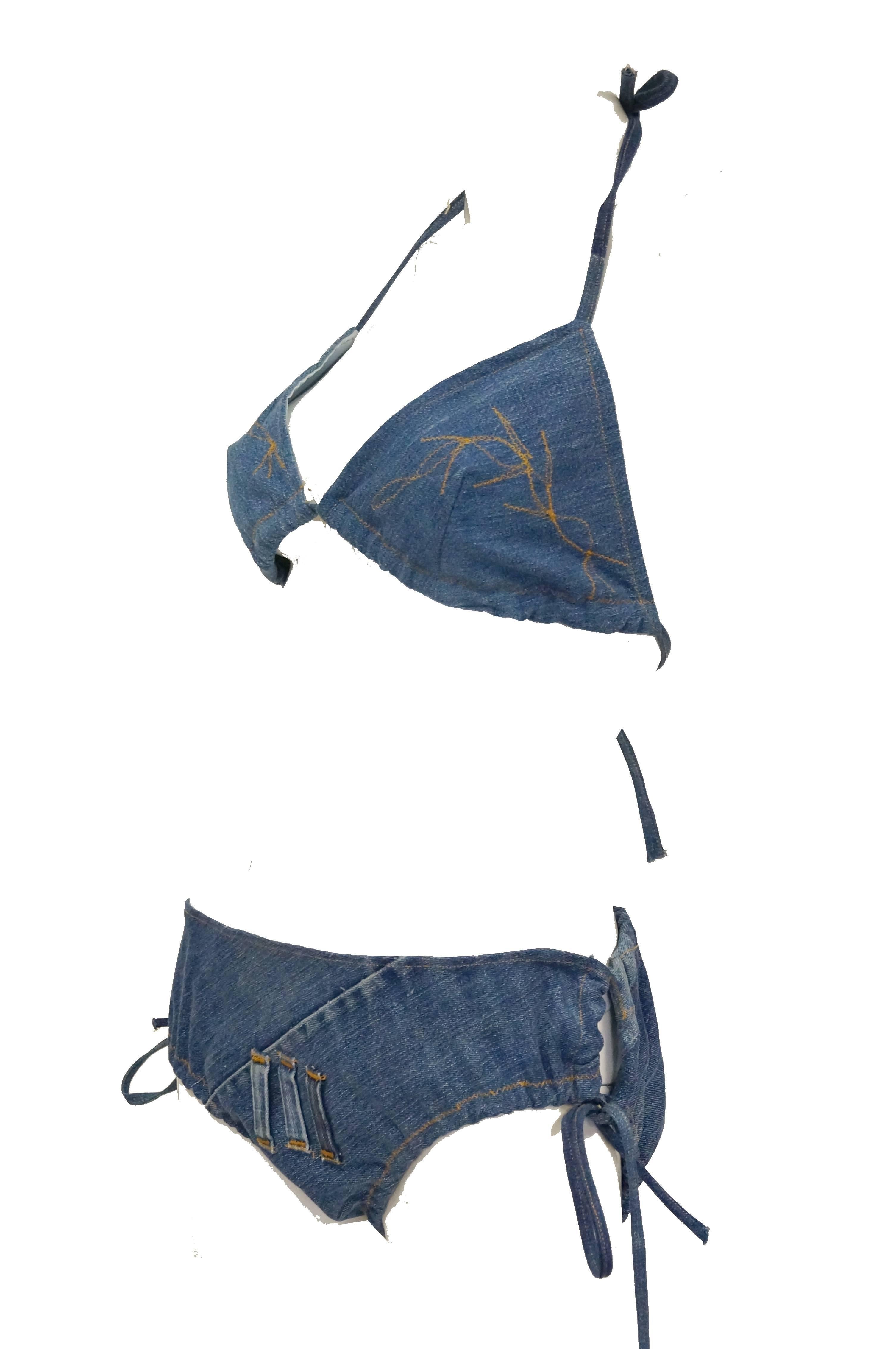 1970s medium wash denim string bikini with gold top stitch. Bikini has triangle top with straps and geometric stitch detail. Bikini bottoms have loop tie detail on sides, three belt loops in front (for a leather belt with brass rings - not included
