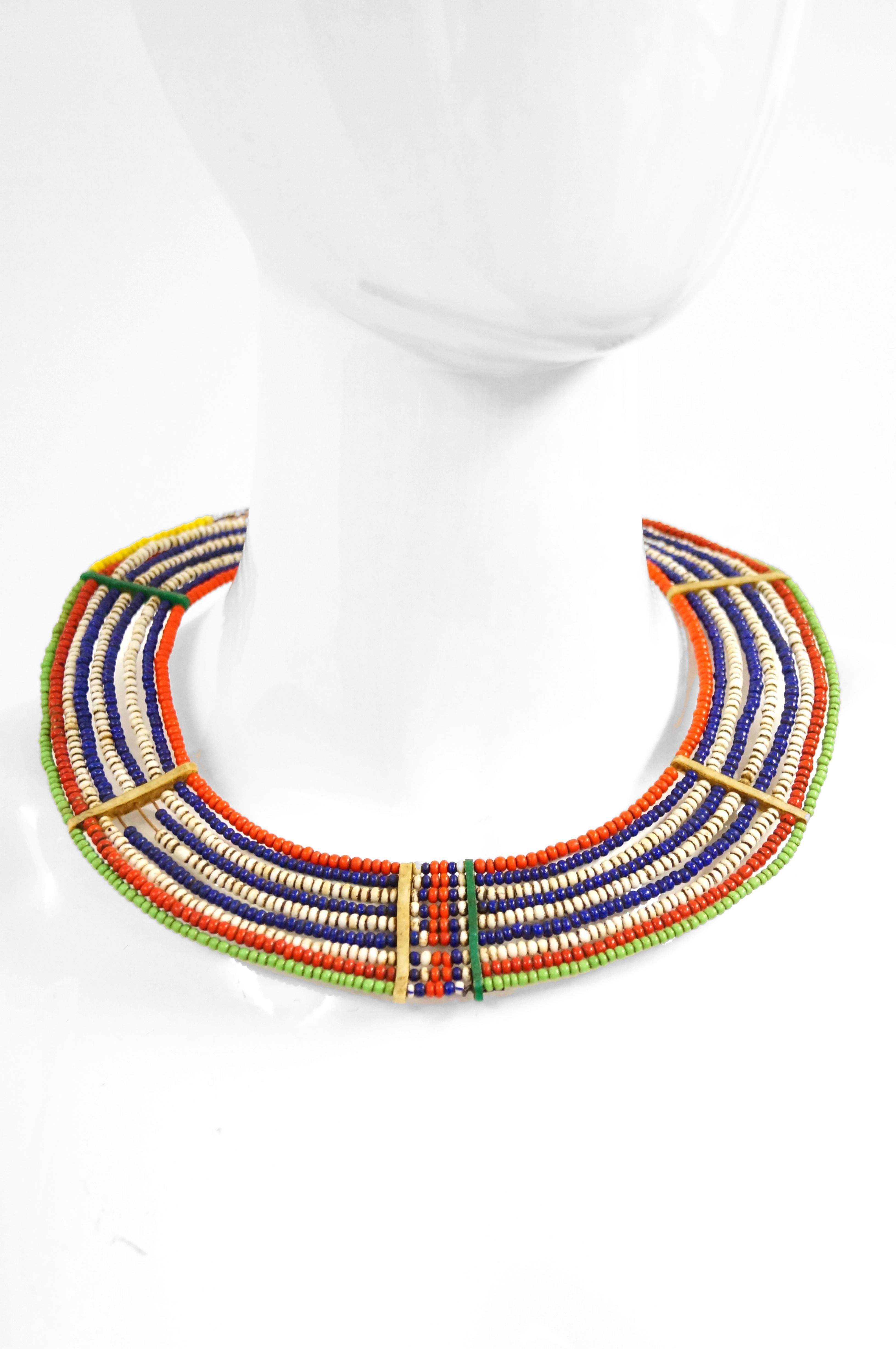 Beautiful colorful circular tribal collar necklace. Necklace is composed of seed beads in red, white, blue, green, and white - blue stripes. Bone bead in center as connecting point. Hook closure.

*Samburu tribe, Kenya.