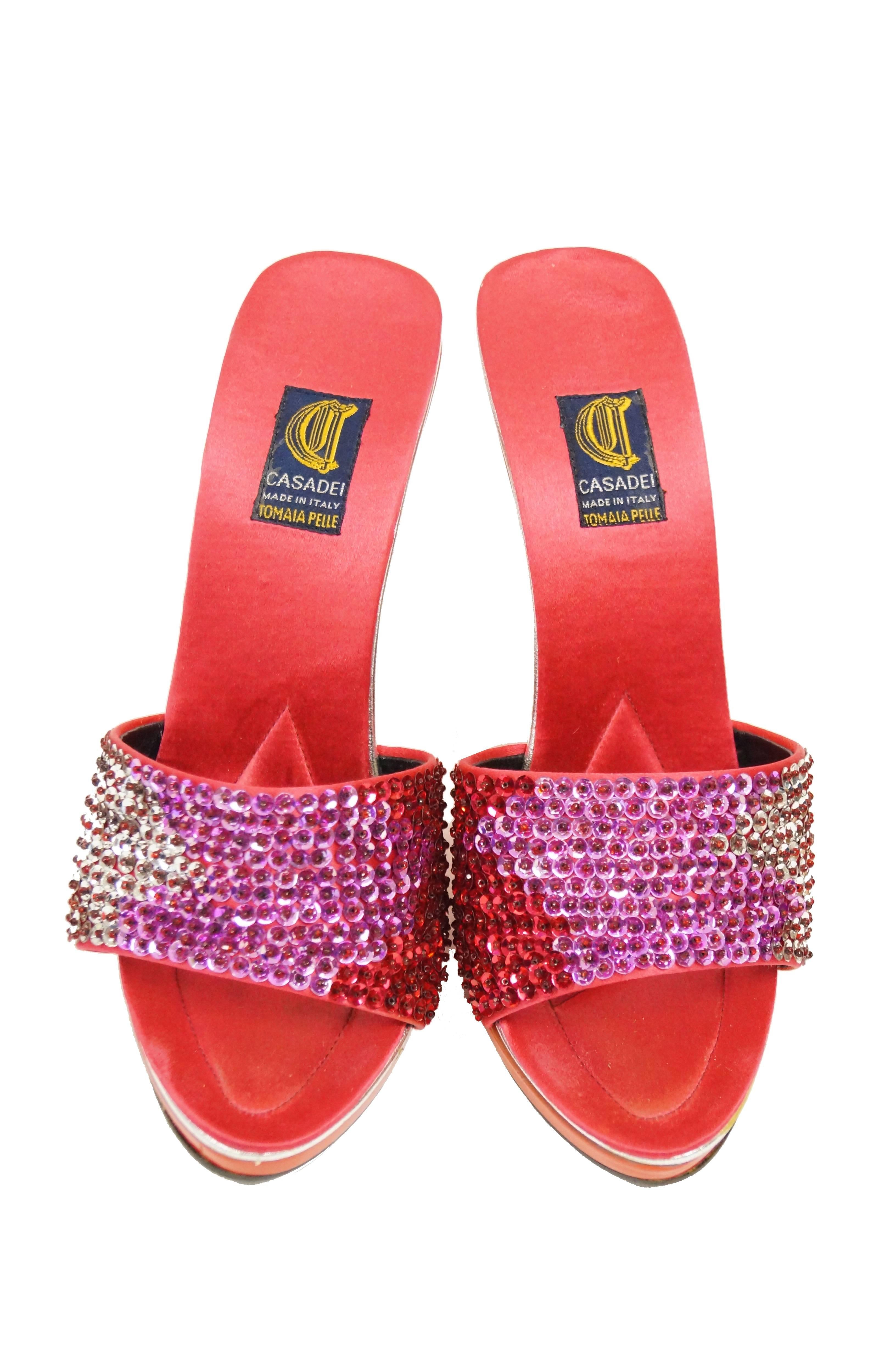 Criss-cross open back sandals by Casadei! The sandals feature thick red satin straps ornamented by red - pink - silver ombre sequins,  a thin, tapering heel in glossy red, and a peep toe. Silver accent stripe running below the satin insole.