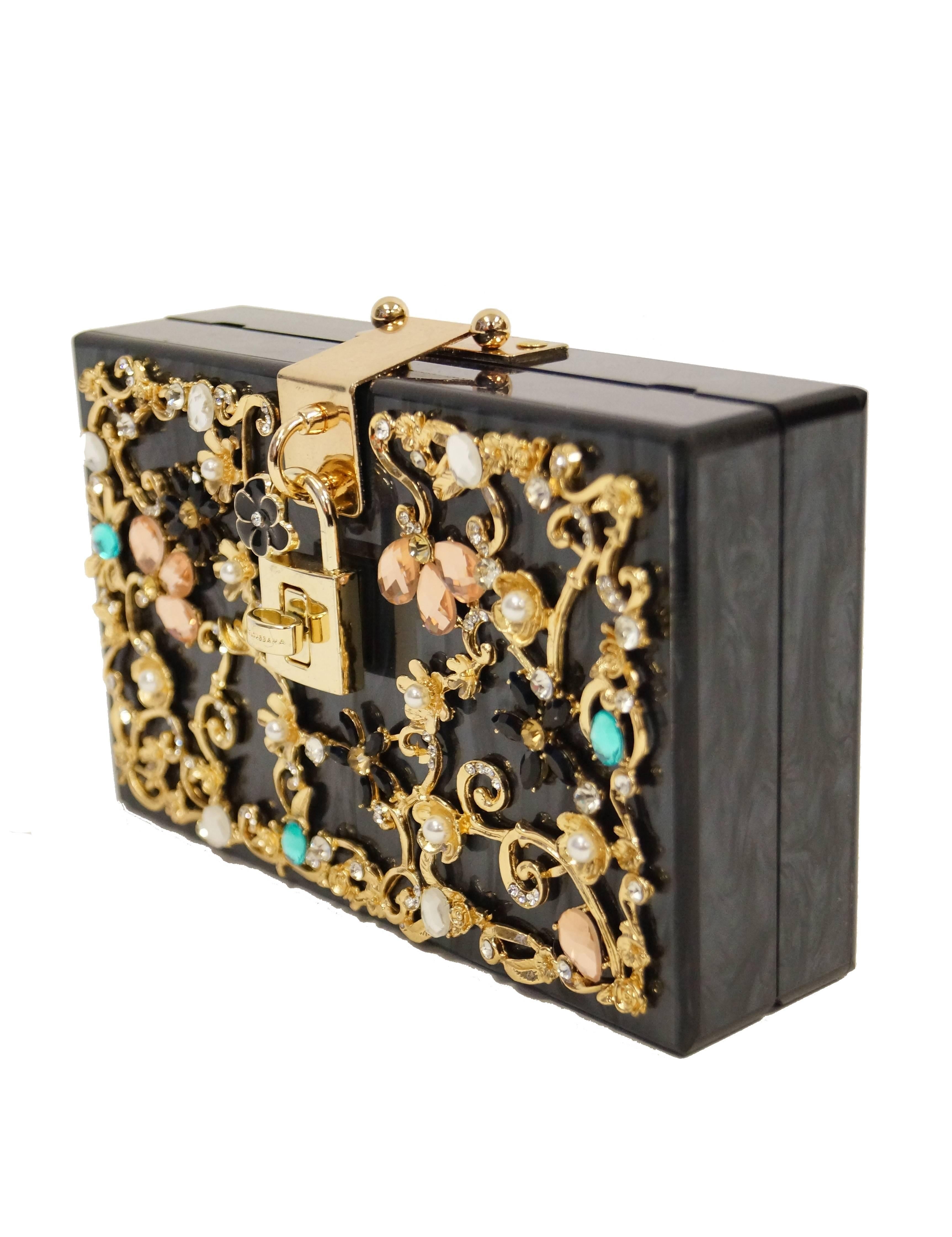 A refreshing new take on the beloved lucite box purse! This Dolce and Gabbana clutch has a rectangular pearlized grey lucite body, featuring gold tone hardware with the Dolce and Gabbana flower lock closure, and floral rhinestone designs on the