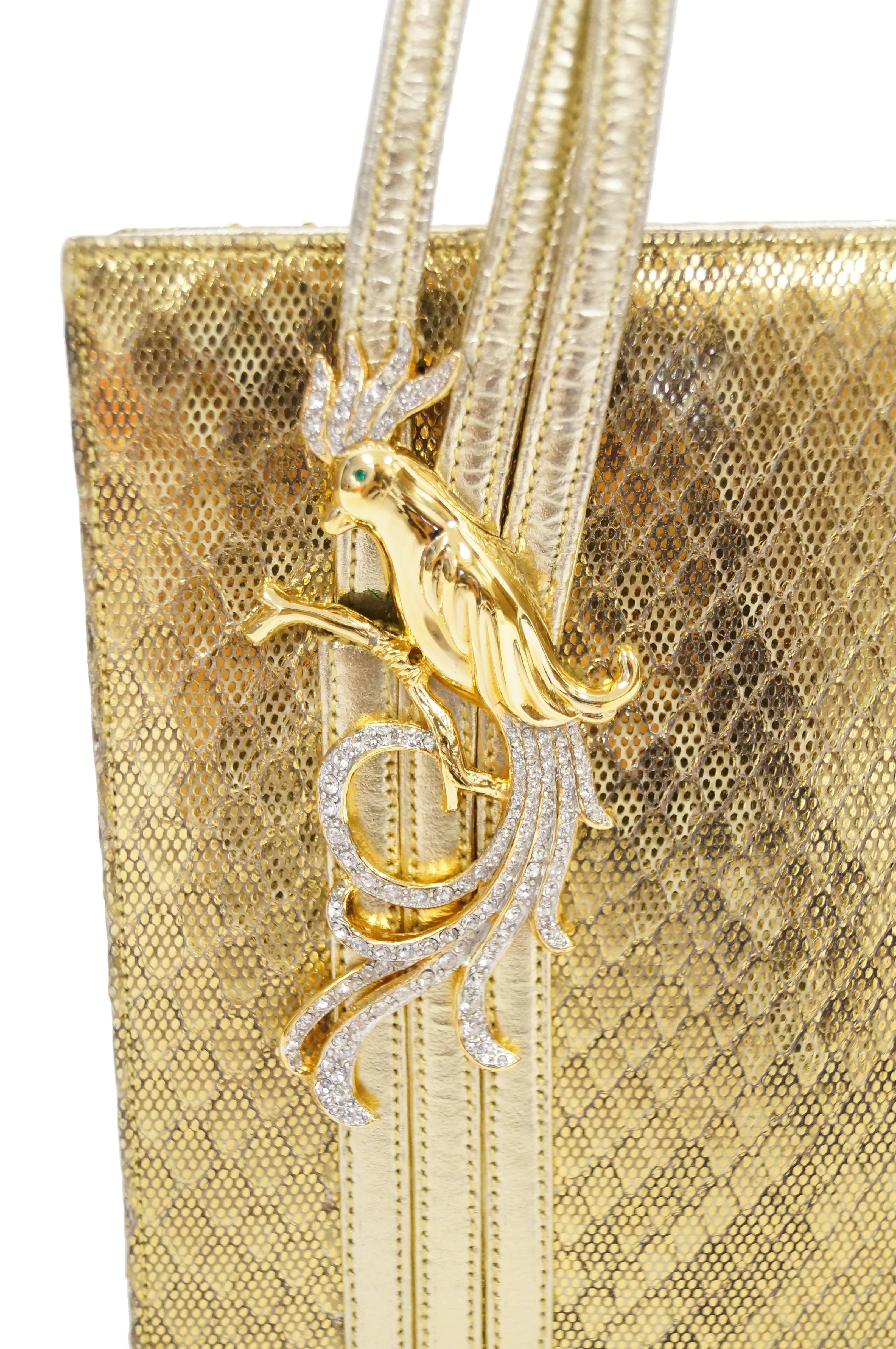 Elegant gold lame snakeskin evening bag by Martin Van Schaak! The handbag has a structured rectangular body, with a triple band handle that loops over from the front to the back. The handle is accented by a gold tone phoenix bird with clear