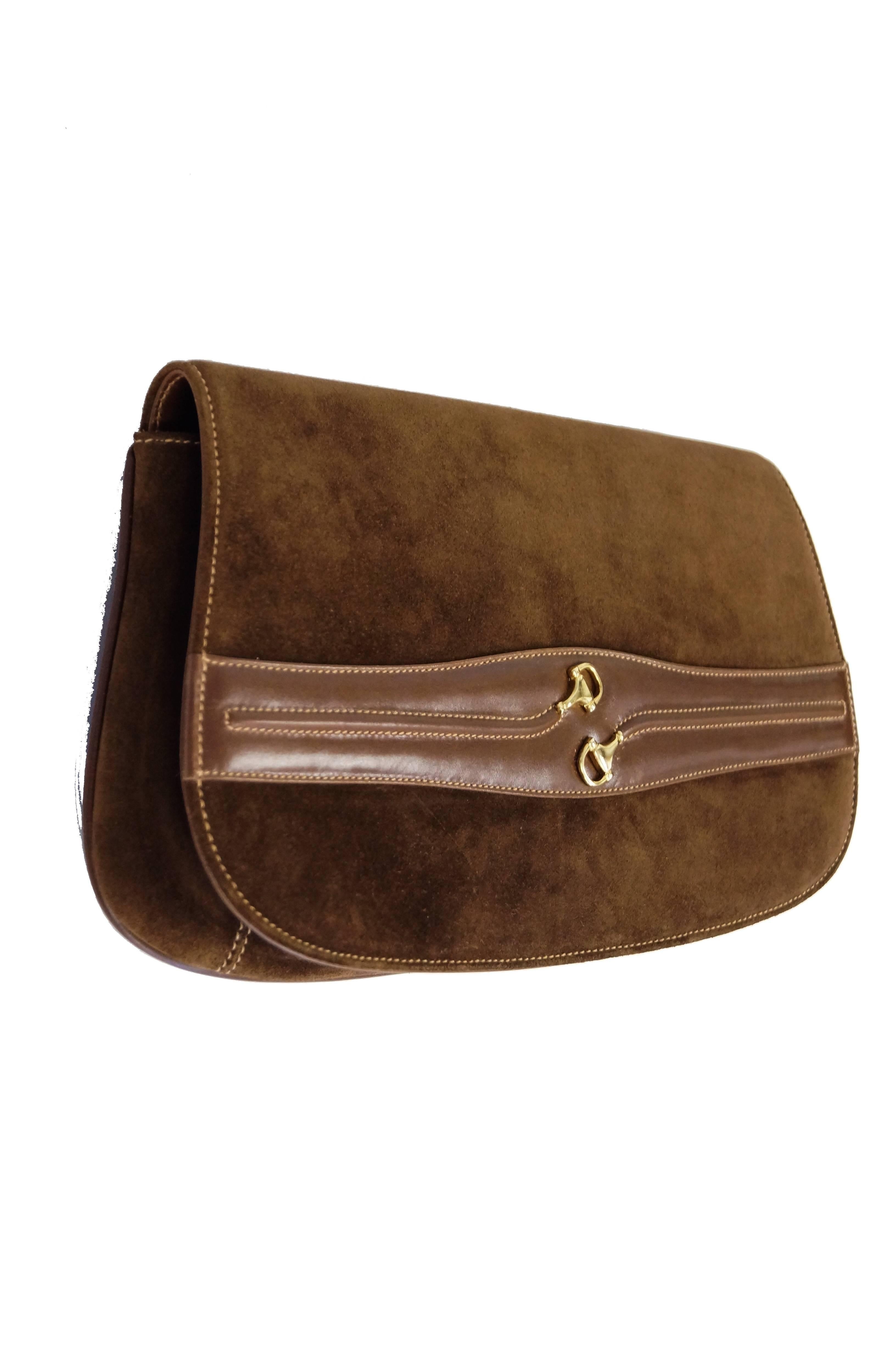 Elegant brown suede clutch by Gucci. The clutch has a rectangular trapezoidal shape with rounded edges (rather like a saddle bag) harkens back to Gucci's foundation as an equestrian leather atelier. The clutch features a strip of leather across the