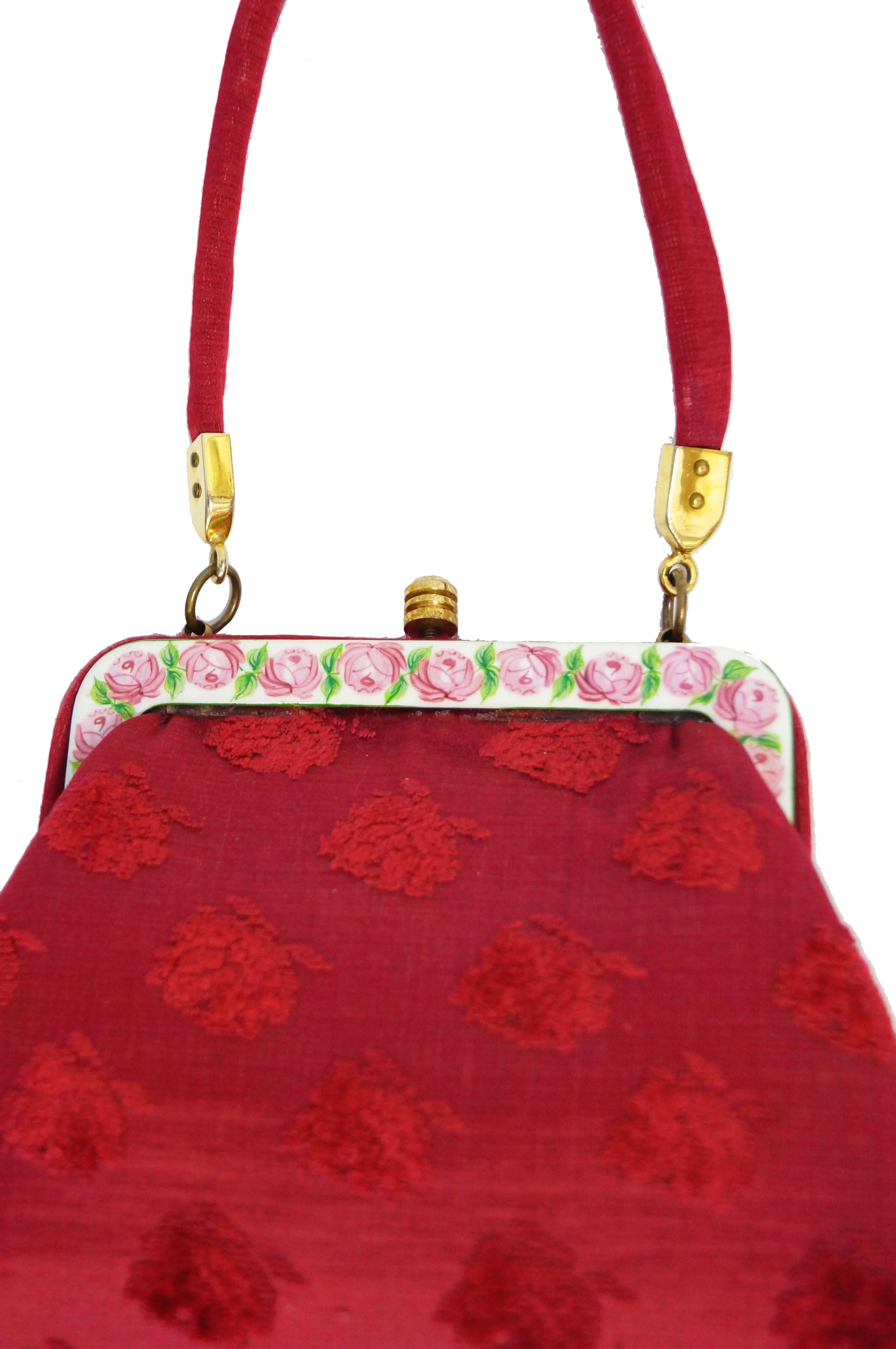 This Roberta di Camerino top handle handbag is composed of a pinkish red flocked floral tapestry structured triangular body with matching thin strap, and a hand painted pink and green floral porcelain closure snap. Gold tone hardware. Handbag has