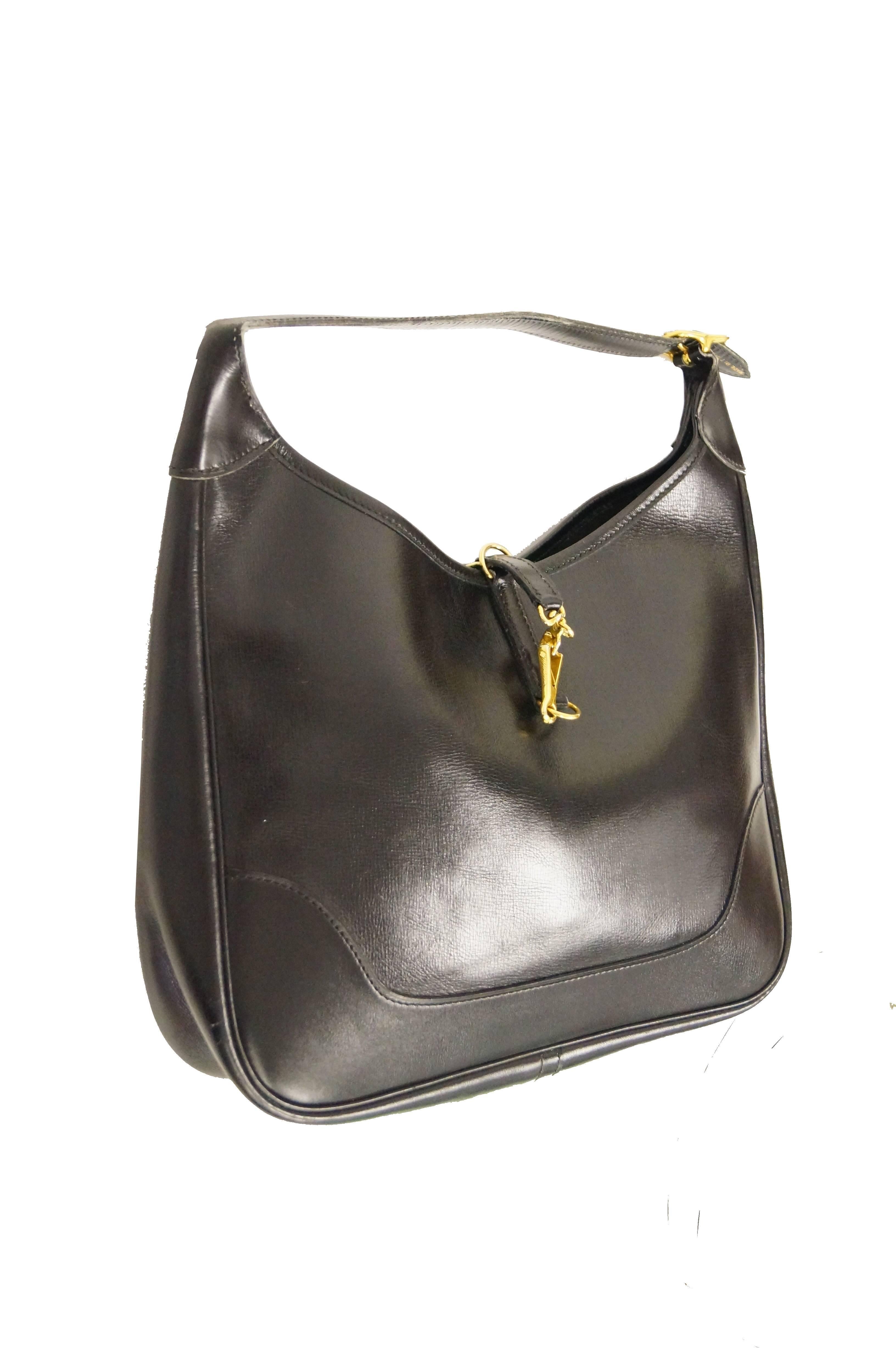Classic glossy black leather Hermes trim bag. This shoulder bag features an elegant, streamlined rectangular body with curved edges and a short adjustable shoulder strap. The handbag has an open top with single pressure lock lobster clasp closure.