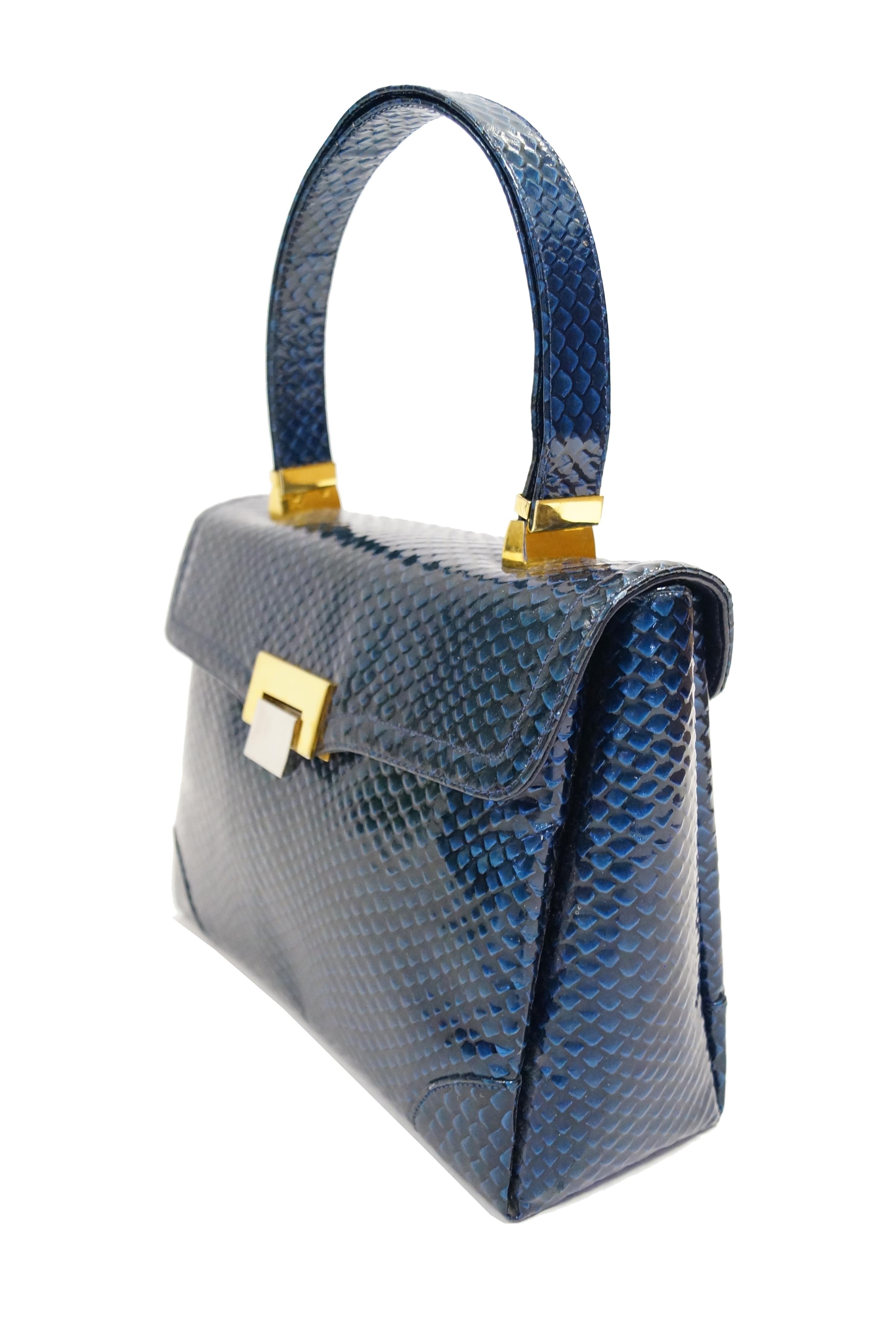 Amazing glossy blue reptile handbag by Koret! The handbag has an A-frame structure, with a rectangular silhouette and top handle. The handbag flap has a gold and silver tone flip lock closure, and the handle features gold tone hinges. The interior