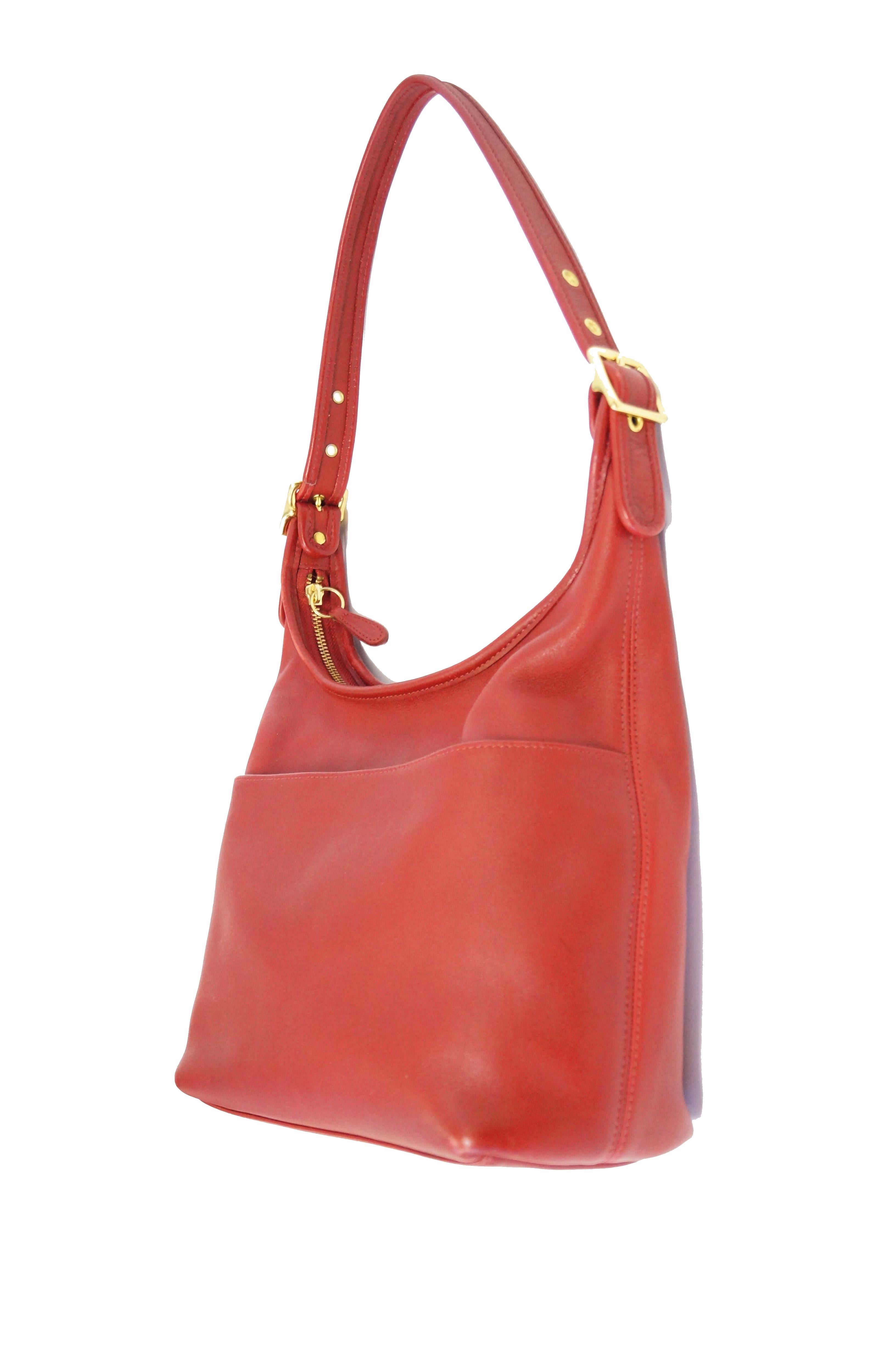 Fabulous reissue of the iconic Coach bag by  Bonnie Cashin! This tomato red shoulder bag features a single deep pocket on the exterior of the handbag, an adjustable shoulder strap with buckle, and a zipper - top closure. The interior of the handbag