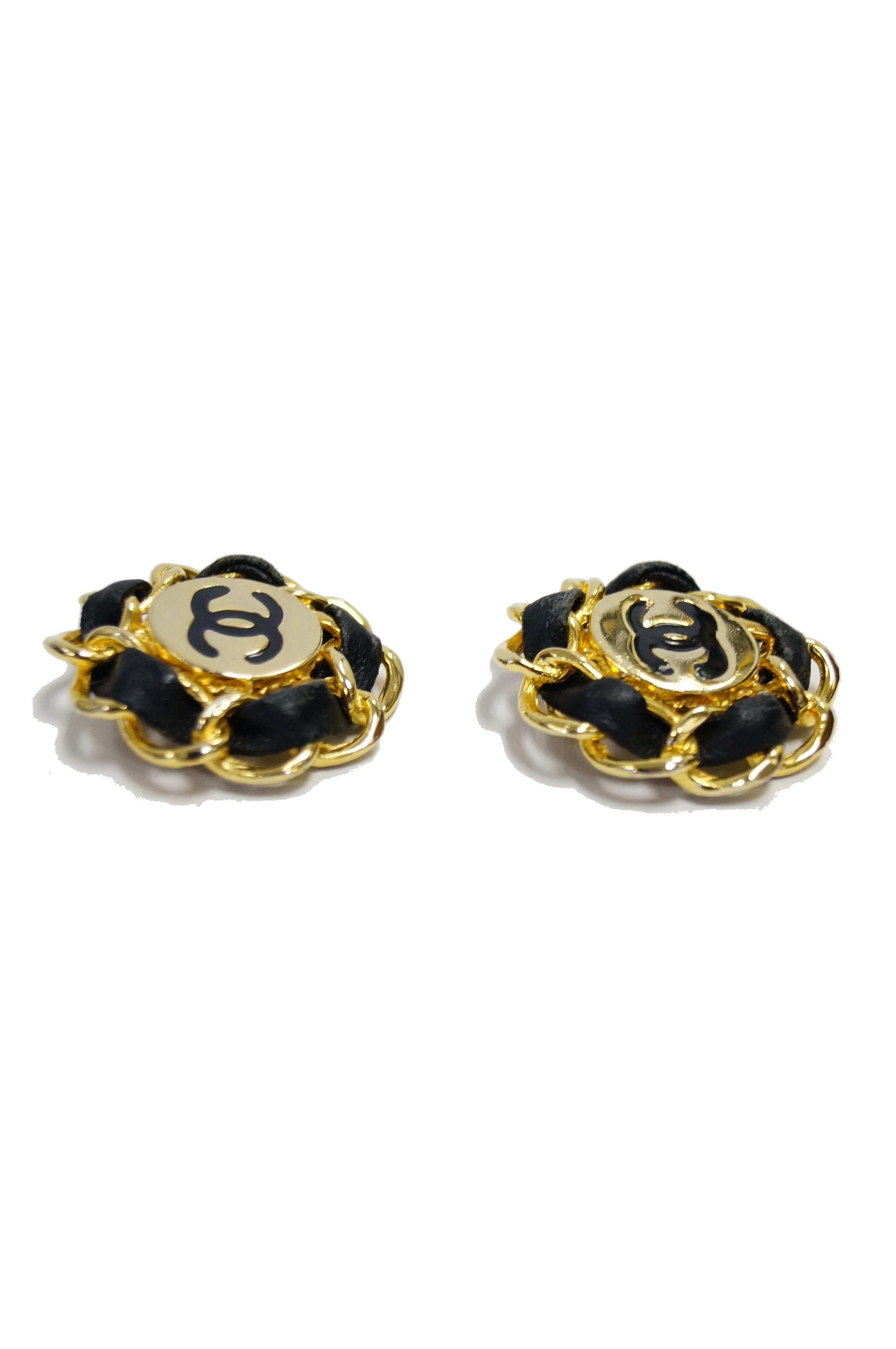 Amazing gold tone Chanel clip earrings! The earrings are circular and feature a chunky gold chain border, with leather woven through the links. At the center us a circular disc engraved and enameled with the famous Chanel linked Cs'. Unmistakably