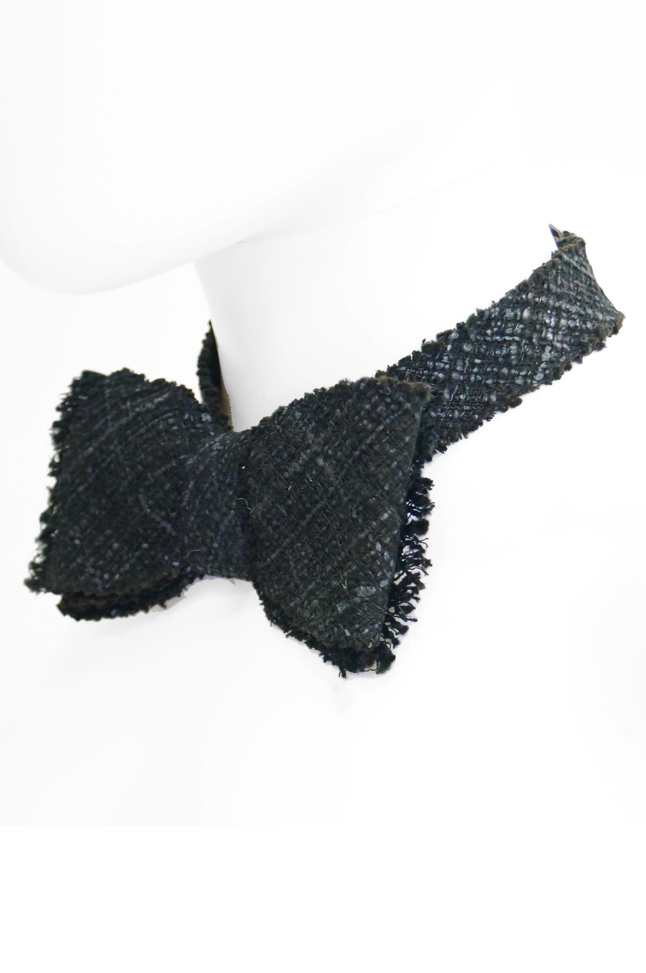 c. 2000, Chanel black cotton and viscose tweed bow tie. Large 5 x 3 inches bow. Fringe on each end of bow. Cinches at back of neck with black metal tri-glide slide. Adjustable. 19 inches end to end neck strap. Fits 14-16