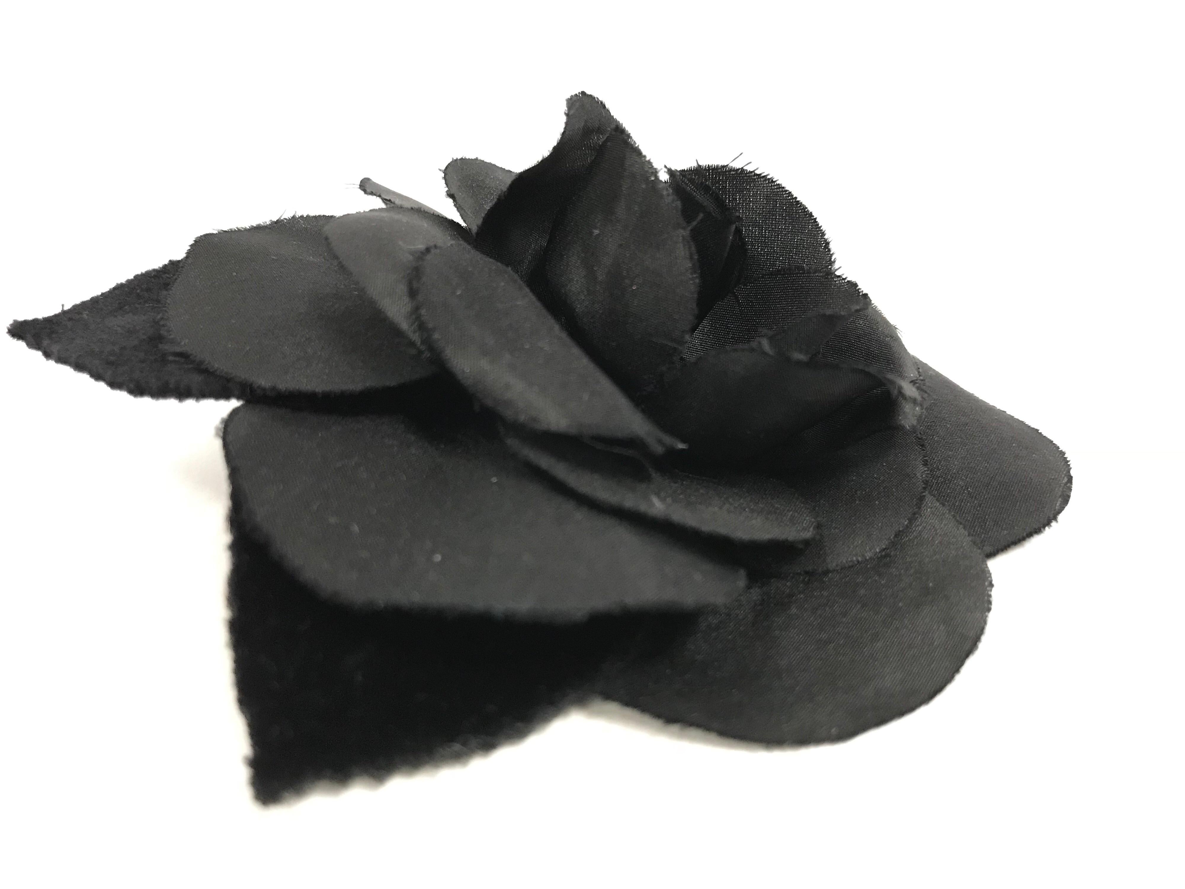 Elegant silk and velvet camellia brooch by Chanel. The black floral brooch is composed of a fabric camellia made up of multiple layers of silk petals, backed by two camellia leaves. There is a pin clip on the underside of the brooch, as well as a