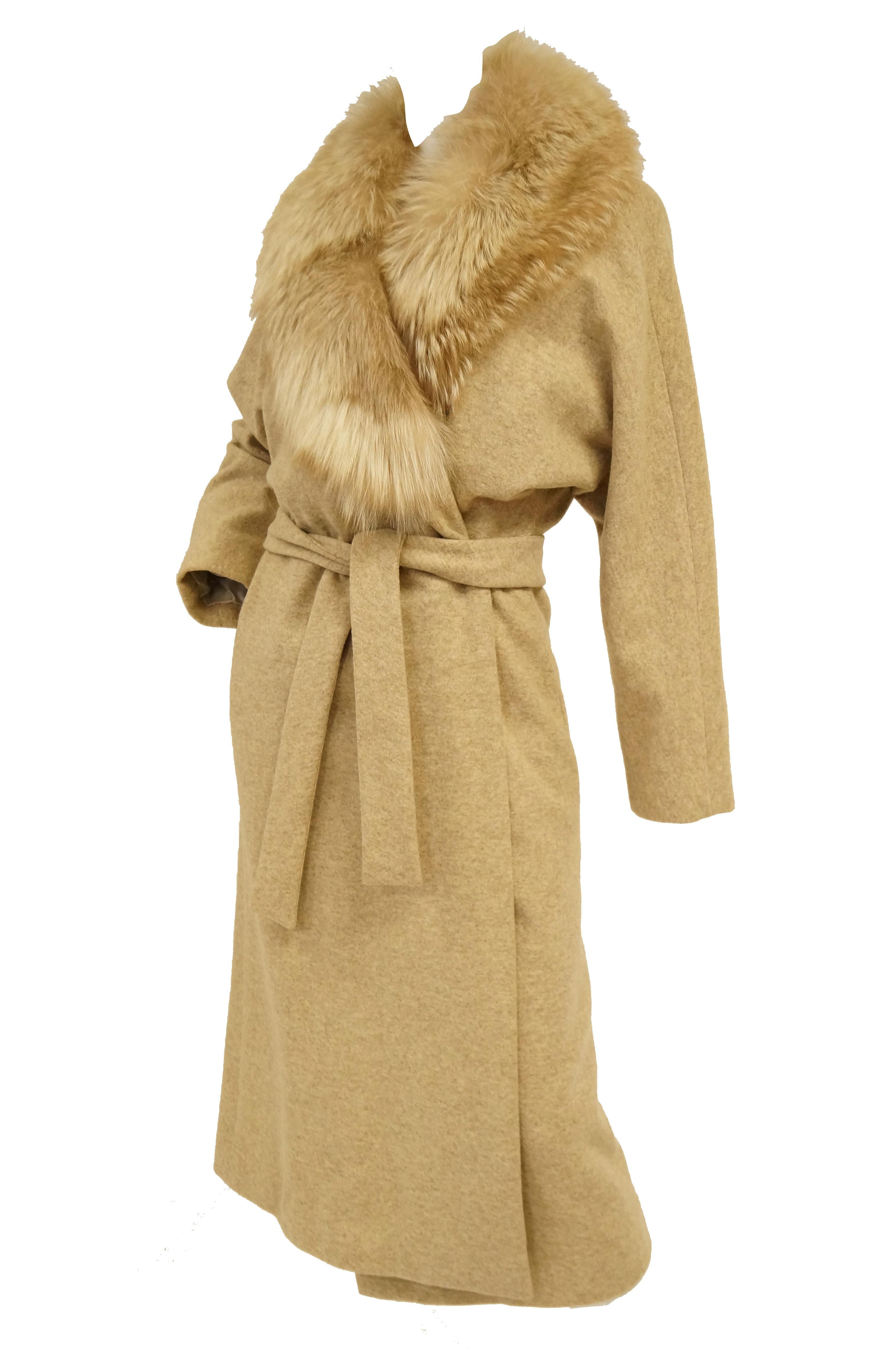 Amazing camel beige wool coat by Bill Blass! The coat is midi length, with long sleeves, a luxurious fox fur shawl collar, and a wrap style closure with matching wool belt. The fur collar is composed of plush golden fox and falls down to the waist