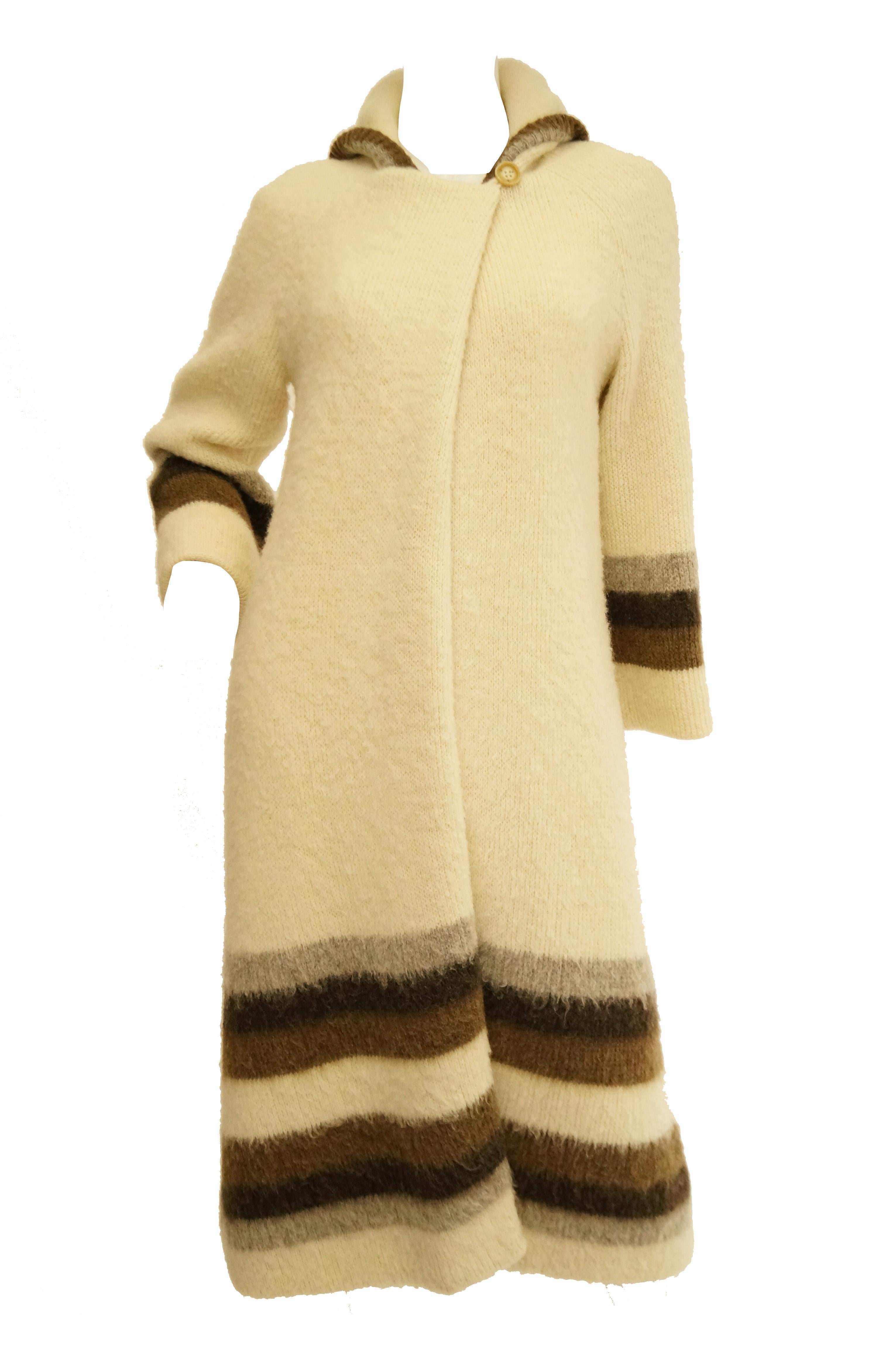 Beautiful and warm cream wool coat by Hilda of Iceland! This cozy coat is halfway to cardigan, falls at around knee length, has long sleeves, and a hood. The coat has a right - over - left Horn button closure at the neck with a free falling front.