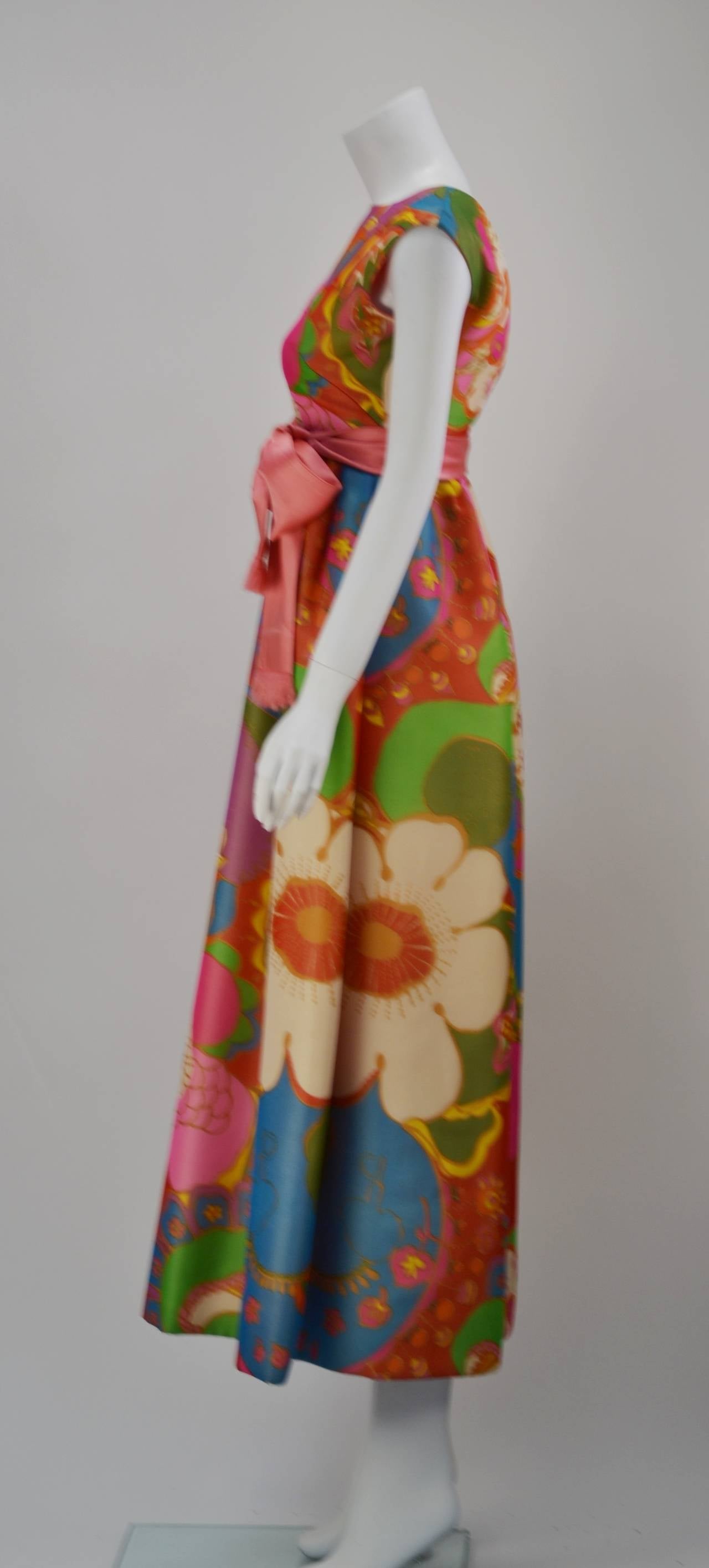 Exquisitely well made late 60's/early 70's maxi gown. This winner boasts a bold and floral print with large flowers that were printed on sheer silk crepe de chine over silk duponi. Lovely coral silk satin sash with fringe adds accent at the