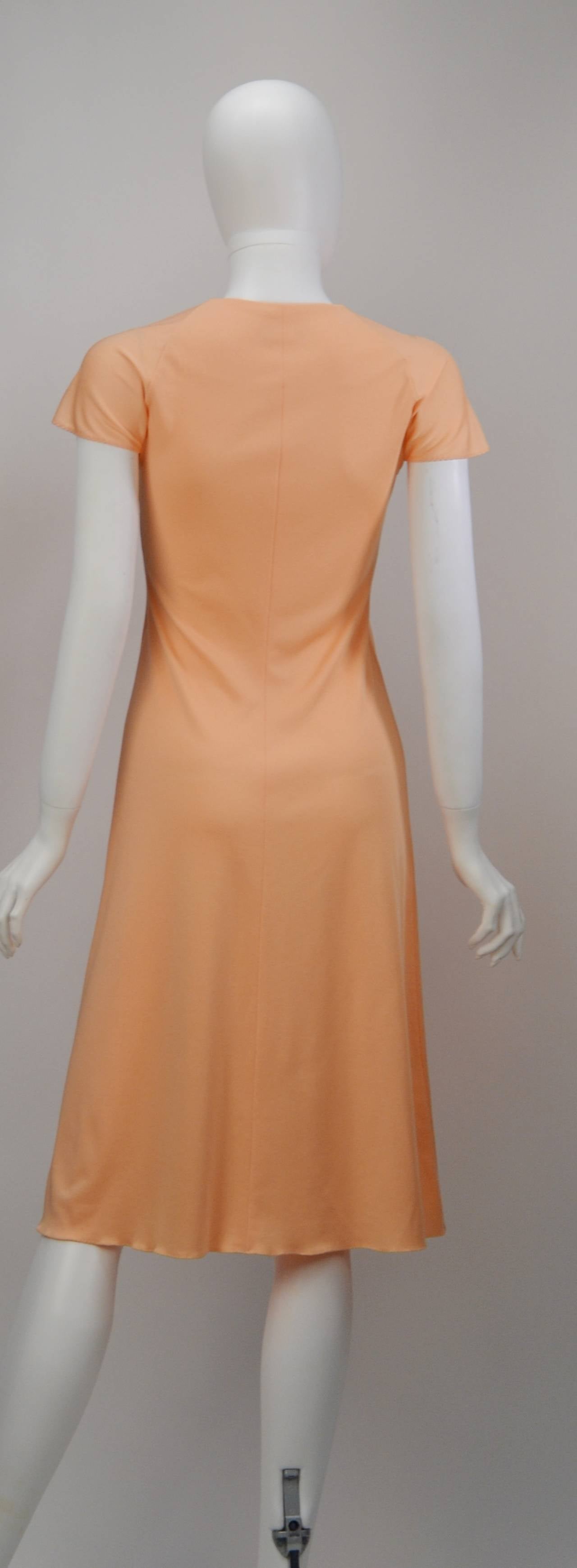 Few, if any, designers can make the color peach look sexy.  Not true of Stephen Burrows, who is the master of simplicity and sex appeal. This gorgeous knee length knit dress dons a loose cap sleeve and tie detail.  Cascading tie end flows down the