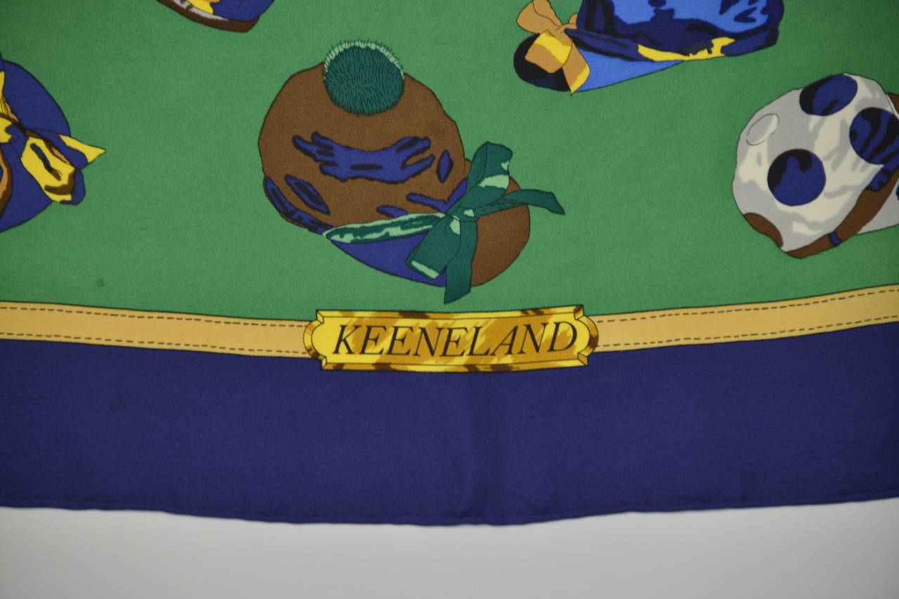 Lovely Ledoux designed Hermes Paris 100% silk multi-color equestrian scarf with original box. This scarf is celebrating the 50th Anniversary of Keeneland. There is a navy blue border with striking olive green center. In the center are horseshoes,