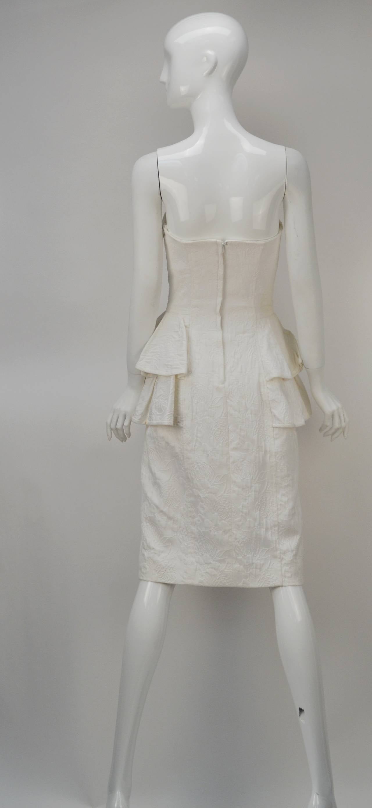 We all need a strapless white dress this summer.  Victor Costa created this elegant yet simple white matelassé dress with side peplums. Decorative buttons on the front. Zips up the back. It has a fitted bodice which extenuates your waist and all