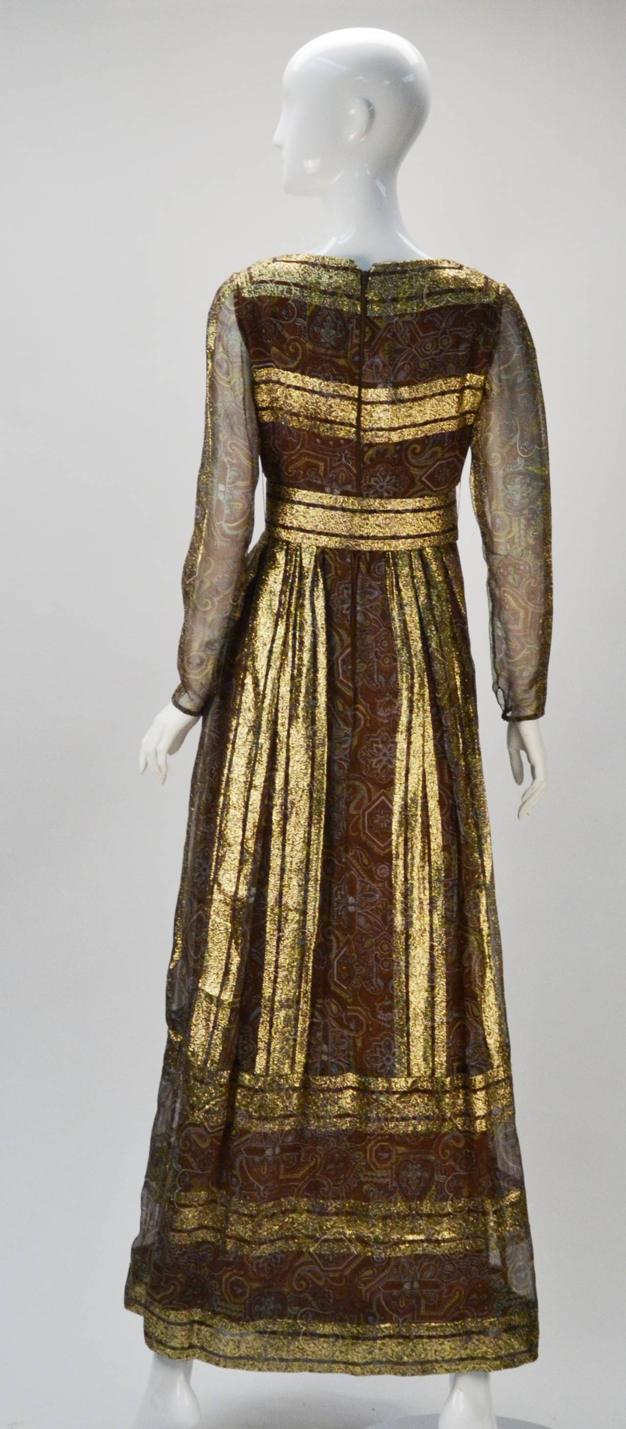 Stunning brown with multi-color paisley print and gold metallic stripes evening dress by Christian Dior - New York Inc. The dress features sheer sleeves with snap closures at the wrist. A wide belt fastens at the waist with hook-and-eyes and snaps.