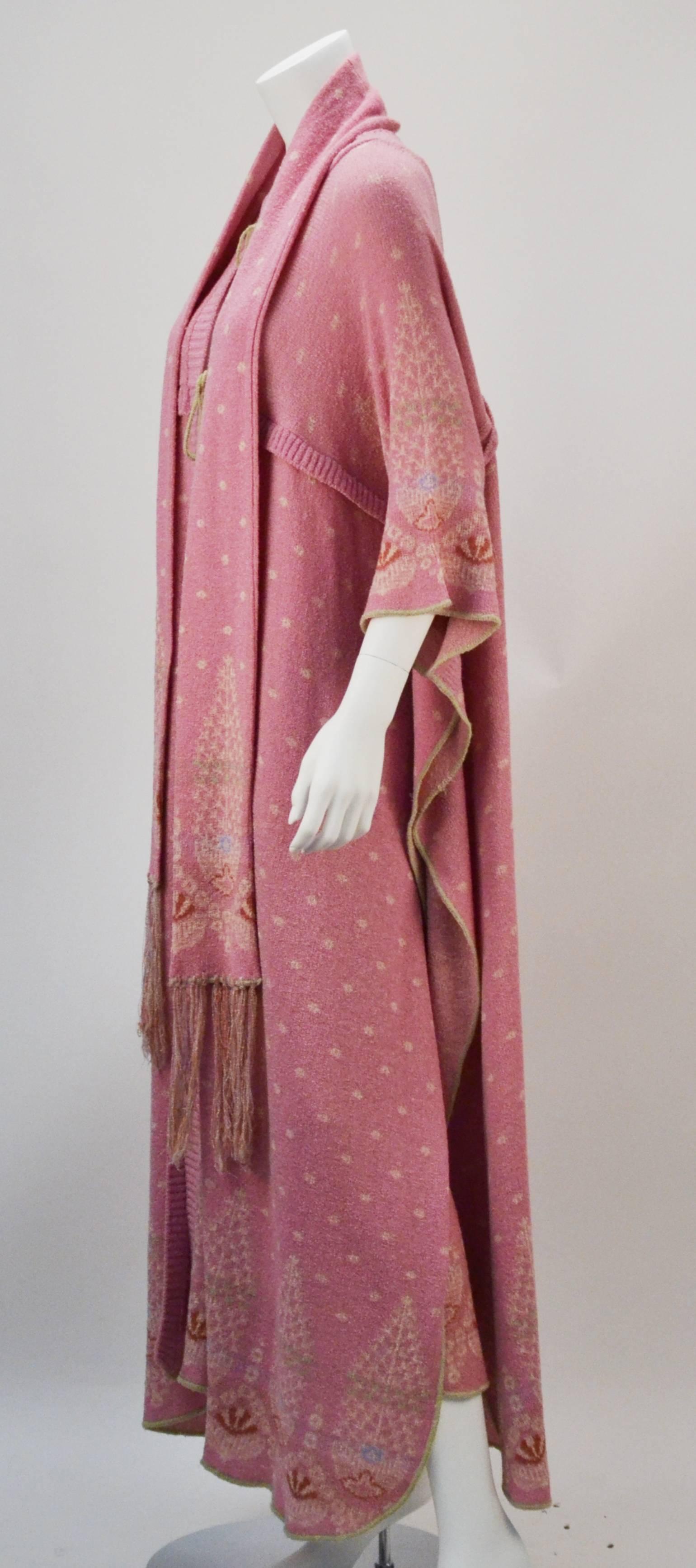 Museum quality 1975 Bill Gibb pale pink knit coat, skirt, and scarf featuring a folkloric-inspired pattern. The coat highlights dramatic kimono style sleeves and ties at both front and back. The skirt has a waistline that ties at one side and a