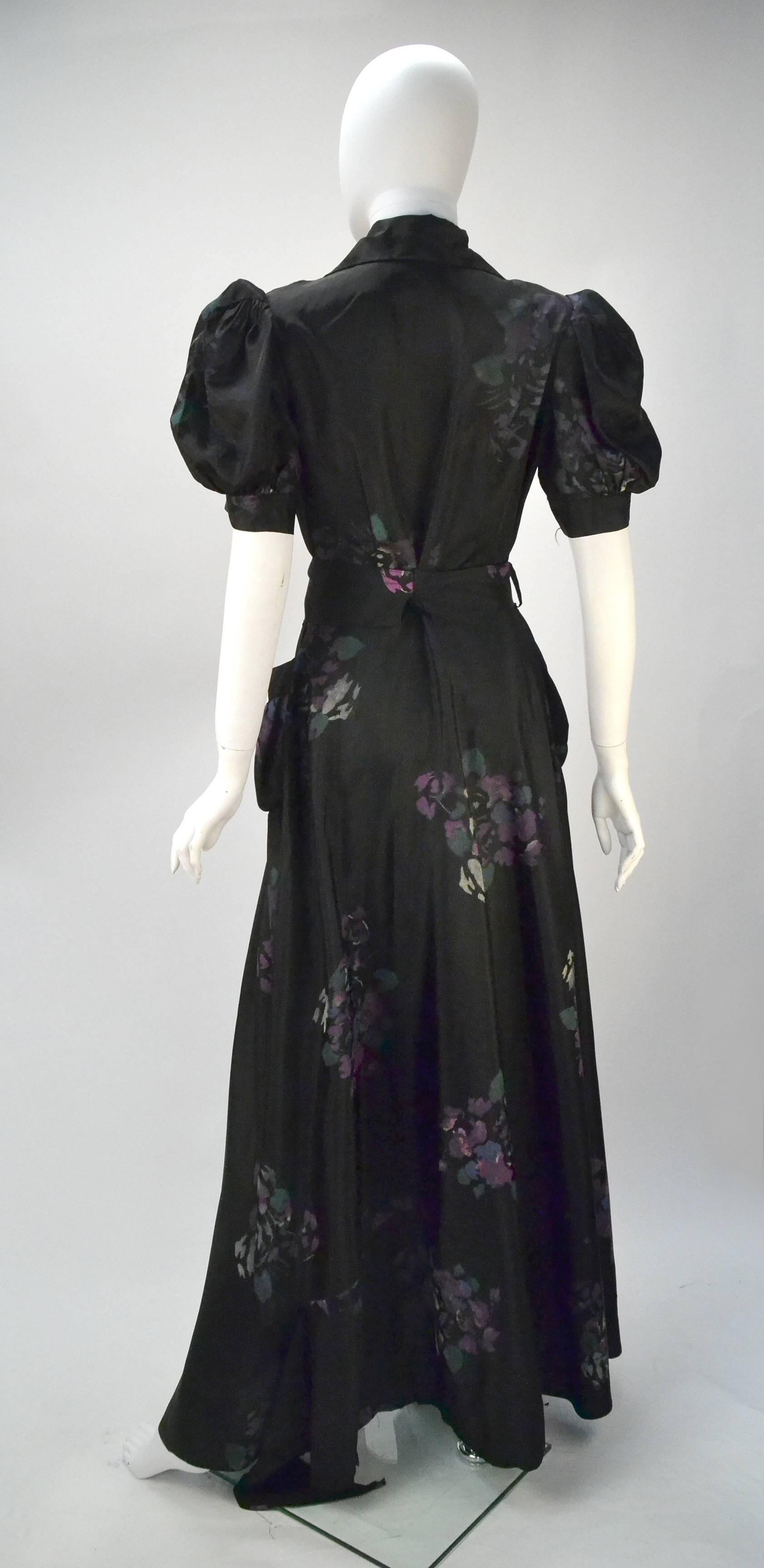 Beautiful 1940's Royal Maid Loungewear black dress with hand painted purple floral bouquets. The dress features puff sleeves, patch pockets and a winged collar. The dress has a front zippered closure. There is a detachable fabric belt for fastening