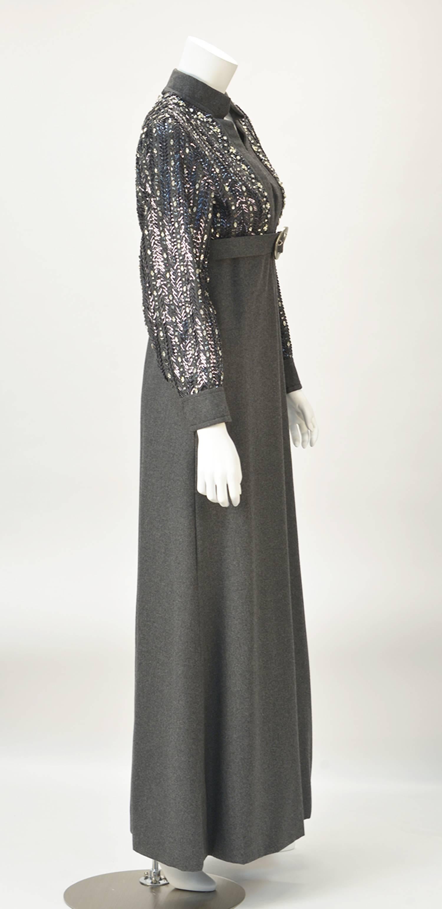 Sophisticated grey knit evening dress with edgy neckline. Long sleeves and bodice embellished with rhinestones and beading. Empire waist and matching grey belt with silver buckle. Just the right amount of sparkle for any occasion! One of our very