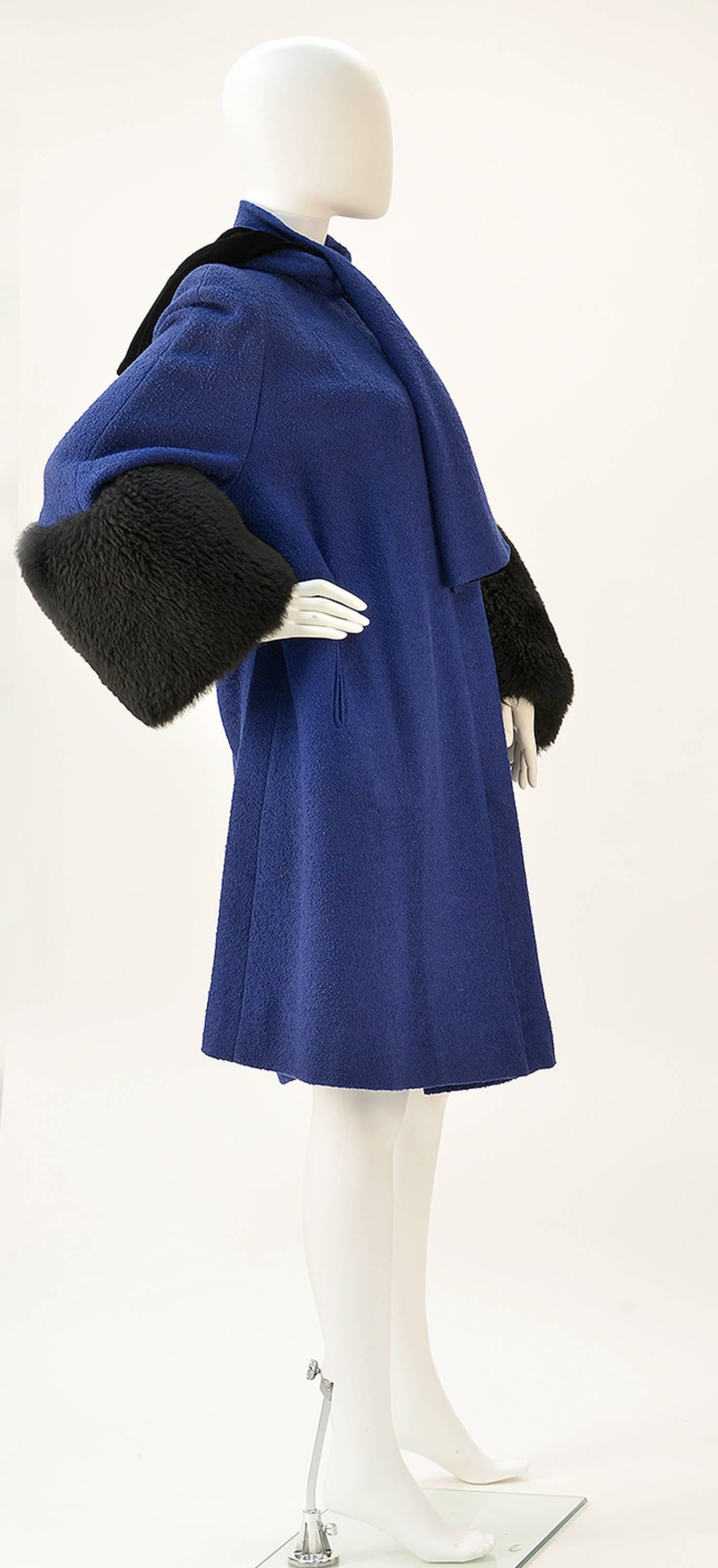 Post- war fabulous blue boucle wool A-line coat made by Julliard. Over sized black lambskin cuffs give an added flair. Sewn in scarf and rhinestone scarf ring attached. Two large button closure. Large side pockets. 100% virgin wool.

Modern size
