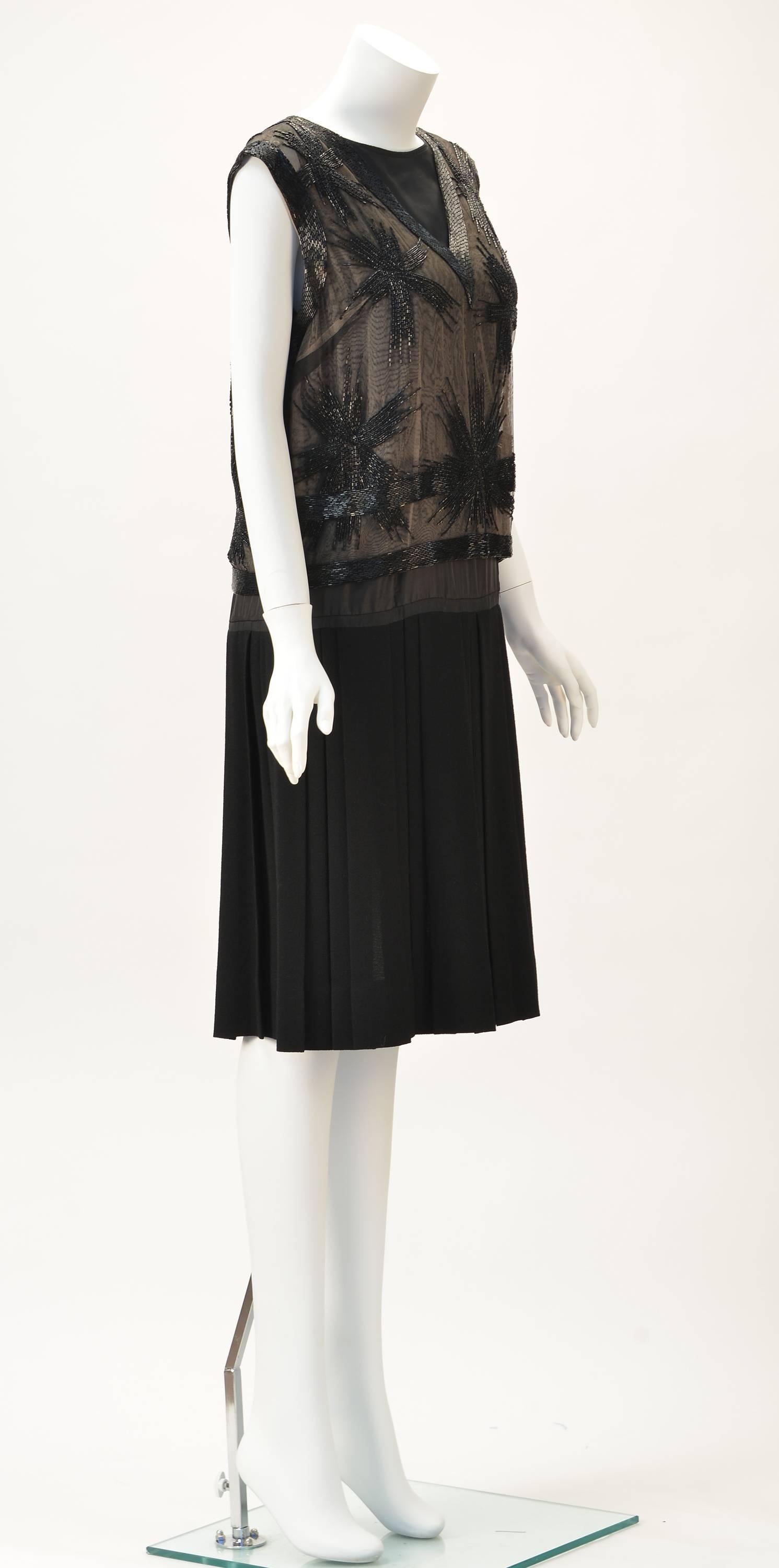 Striking Malcolm Starr black crepe dress with pleated skirt. Sleeveless under-dress with sheer beaded top. The top is nude sheer with hand sewn beading in a star pattern all over. V- neck. Snaps in back. Back closes with hooks and eyes as well.