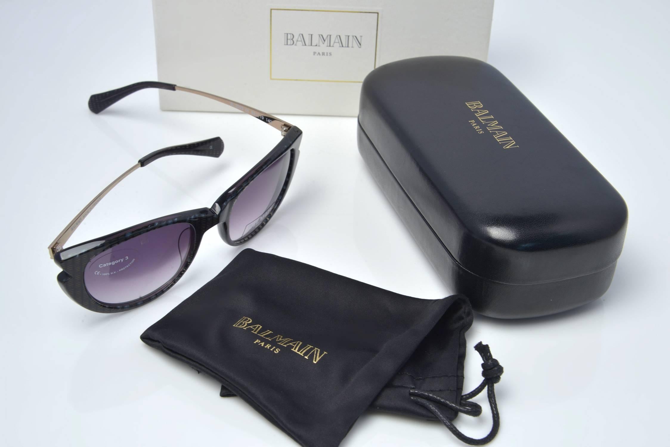 Balmain Paris cat eye sunglasses with case and original box. The main frames are a grey-clear hue with black stripes. The temples are a gold tone metal with the logo.  Lenses are a grey gradient. Also included in the set is a protective pouch, along