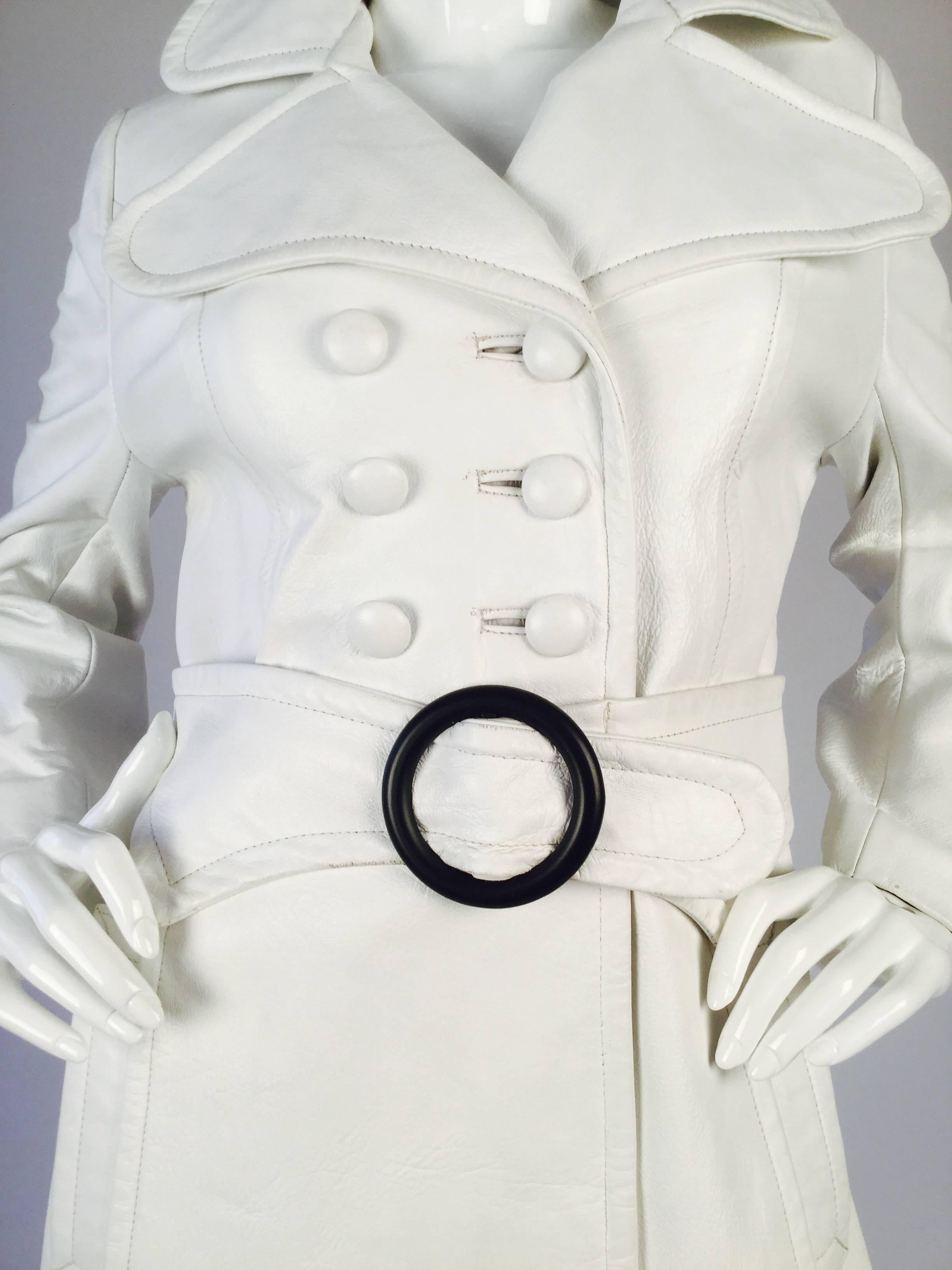 Striking white trench! This 1960s leather trench coat is composed of white leather, and features a slightly exaggerated rounded-edge notched collar and a double-breasted front button closure. The coat has a wide belt attached with large, round,