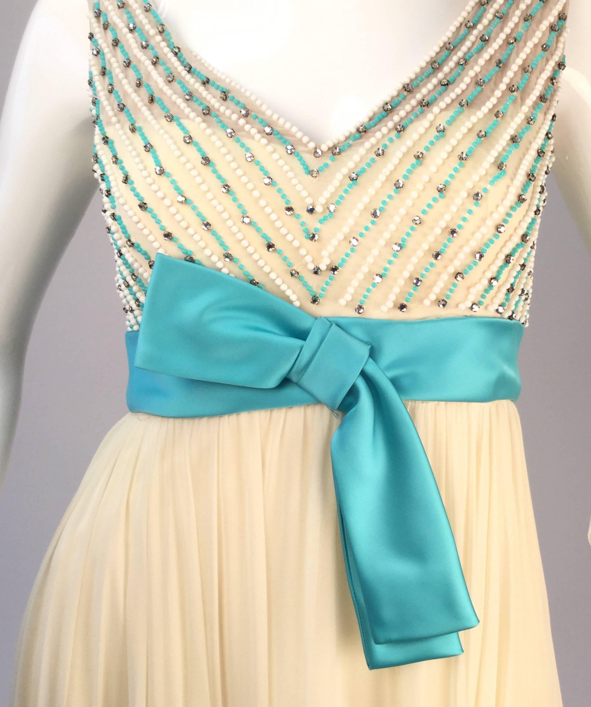  1960s evening gown from historic Houston boutique Isabell Gerhart. This gorgeous cream and turquoise silk dress features a heavily beaded bodice adorned with rhinestones. A turquoise silk satin sash with a bow adds flair to the waist, and closes in