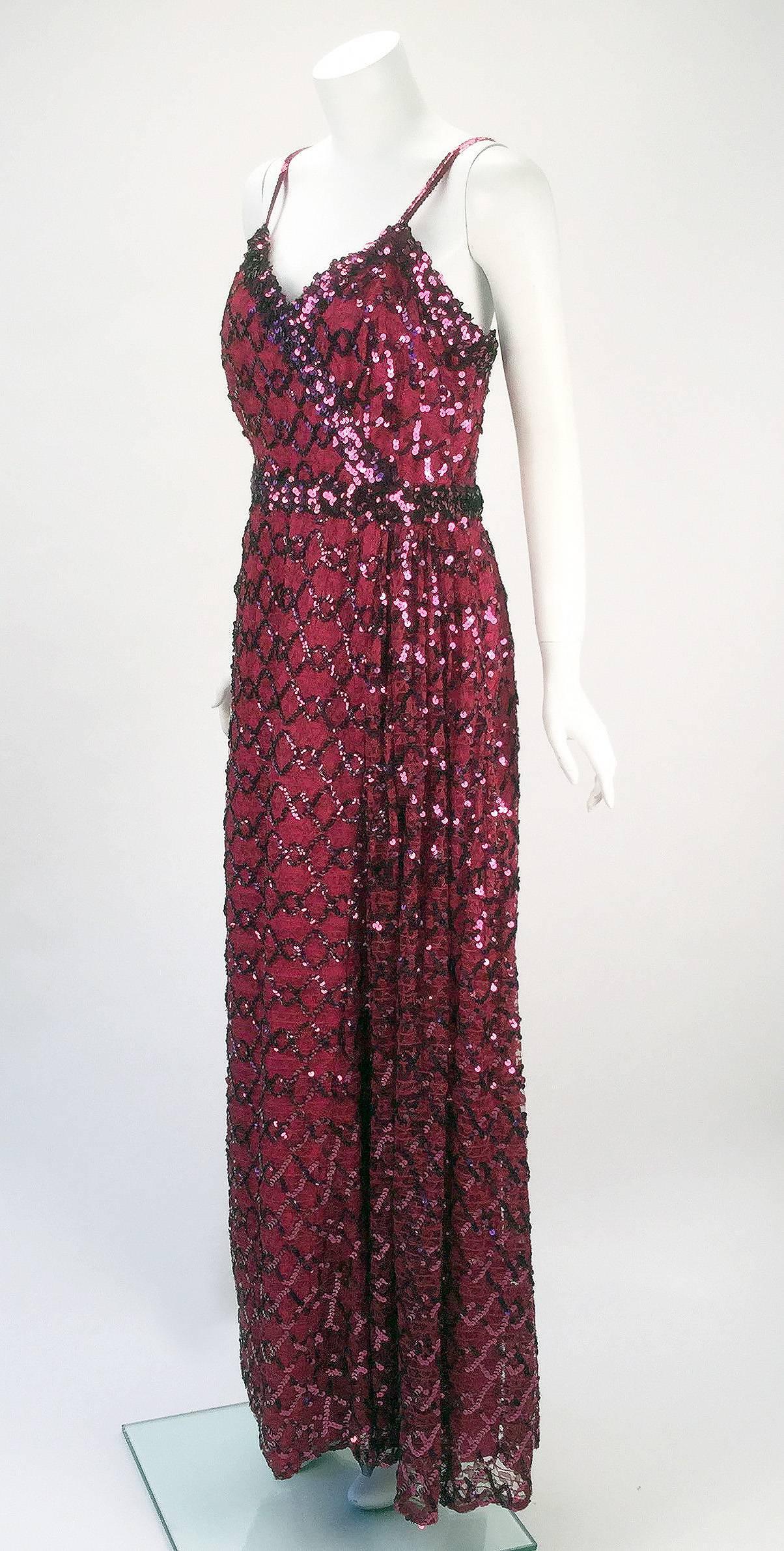 1970s Lilli Diamond maroon sequined evening gown. The sleeveless gown has a surplice-style neckline that is bordered with wide sequin trim. The lace fabric has sequins sewn in a pattern throughout. A detachable sequin belt also sits at the waist and